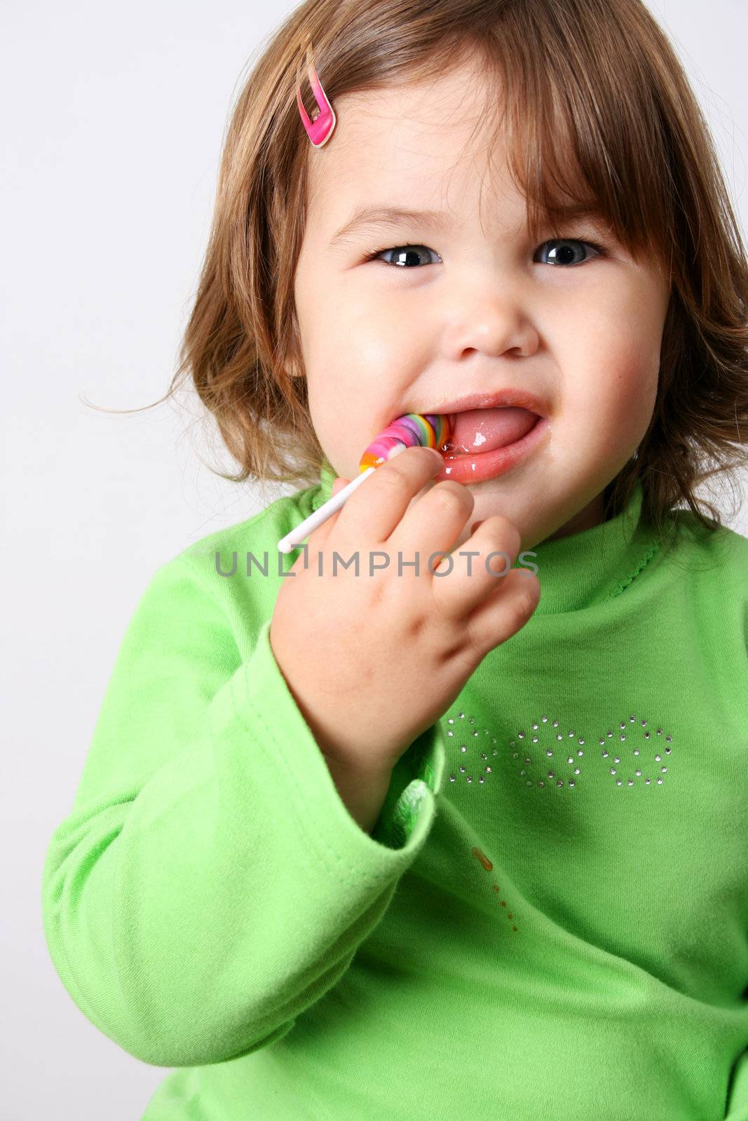 Toddler girl with chubby cheeks eating a sticky lollipop