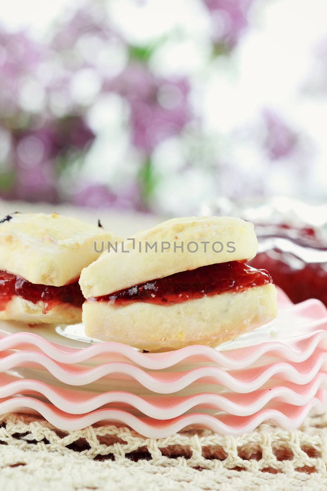 Closeup of freshly baked cranberry scones sitting on an outdoors table with strawberry preserves. Selective focus with shallow depth of field. 