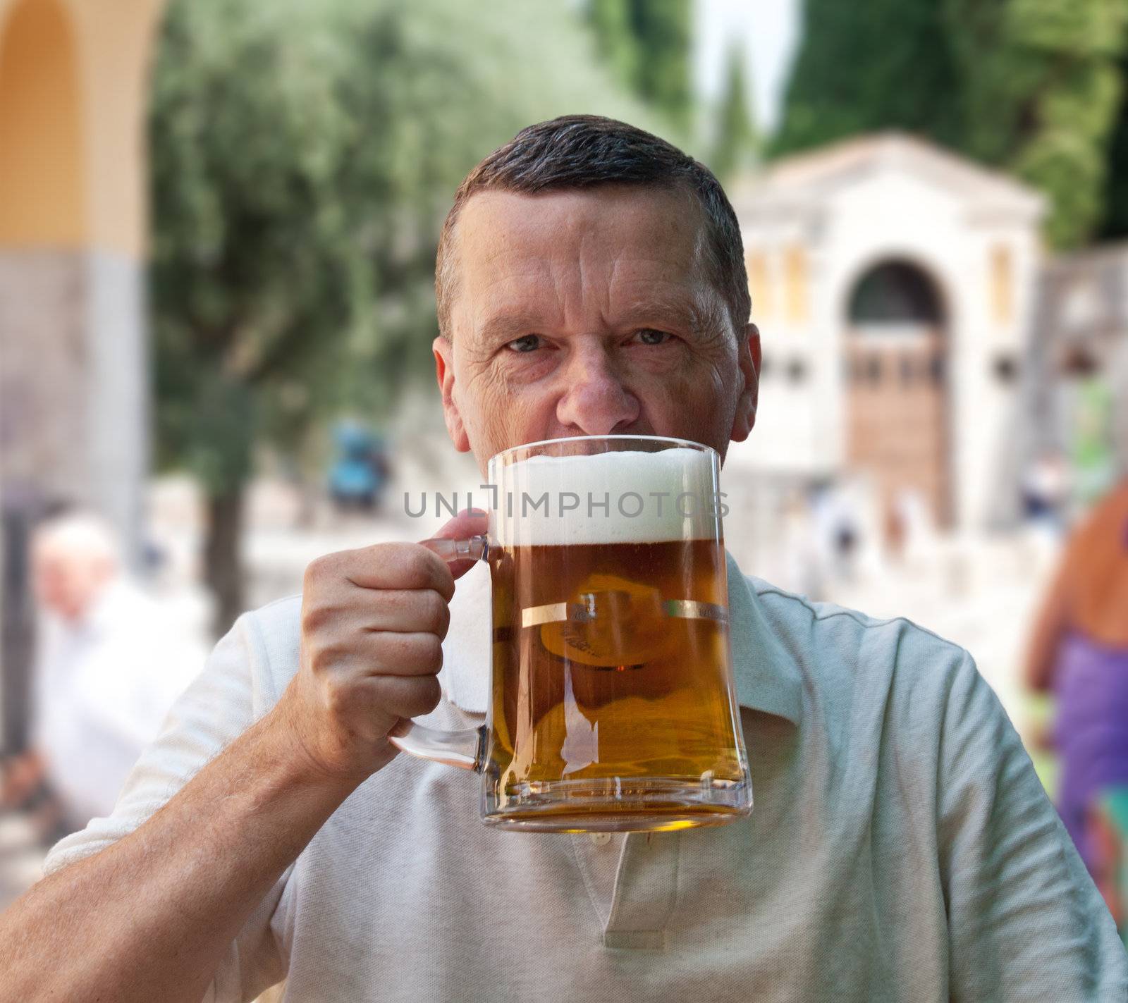 Senior raising a large liter of lager in sunny outdoor restaurant or bar