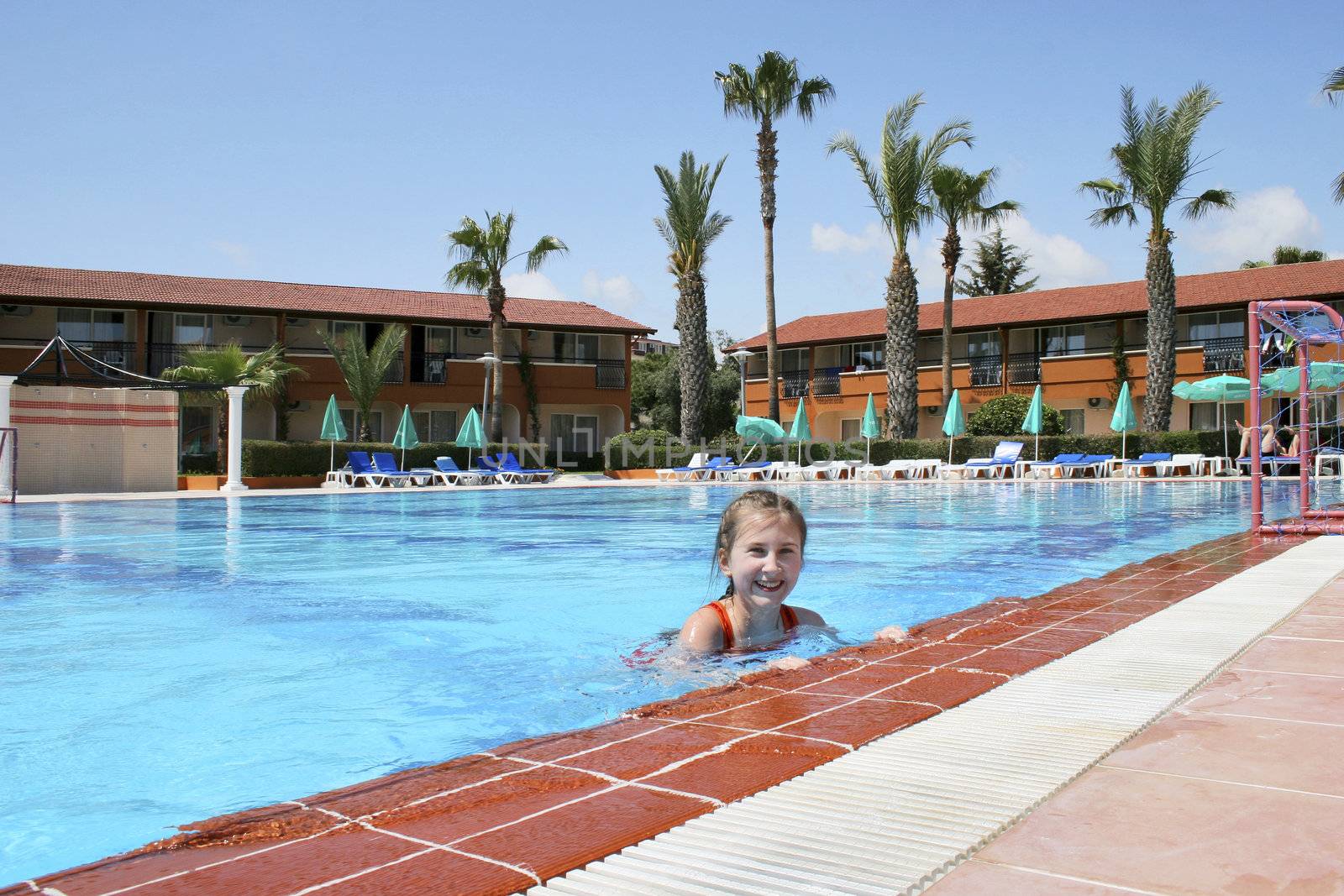 Young girl grinning and squinting as she looks up out of a swimming pool.