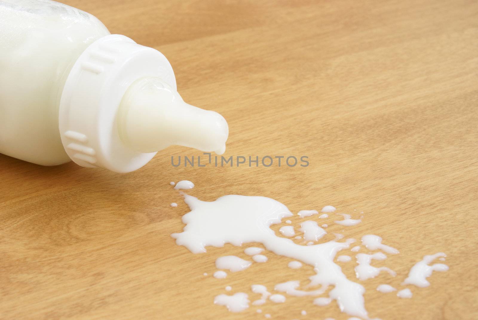 A baby bottle has tipped over and milk has been spilled.