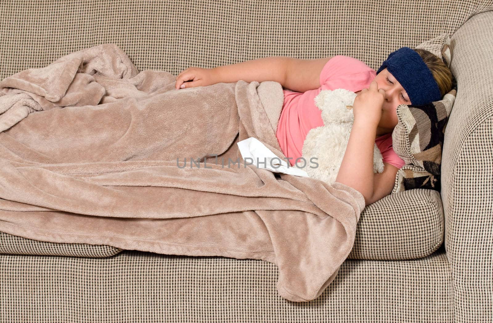 A young girl lying on the sofa feeling under the weather, and enjoying the company of her teddy bear