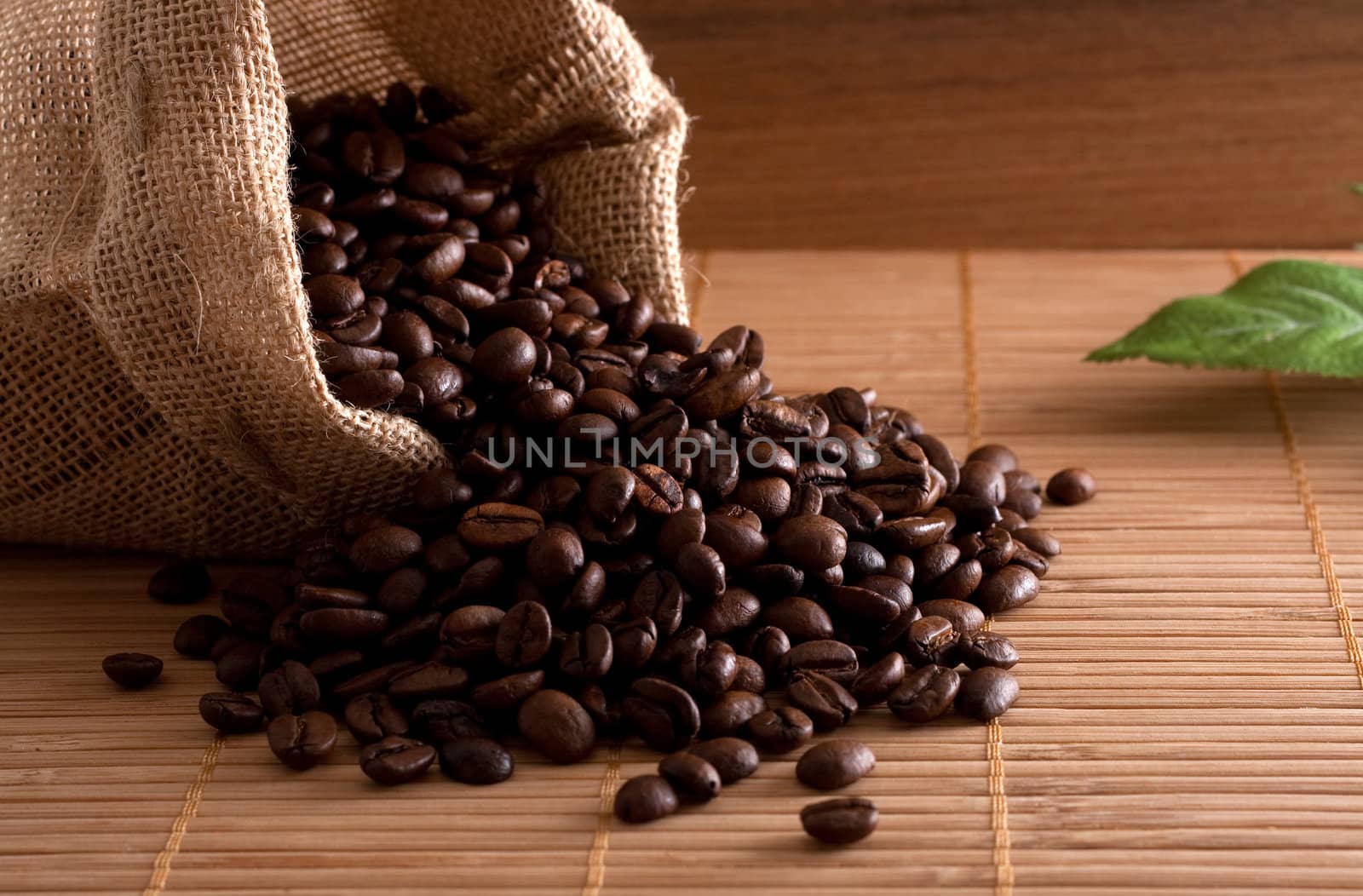 A bunch of coffee beans, falling out of a sack on a wooden background