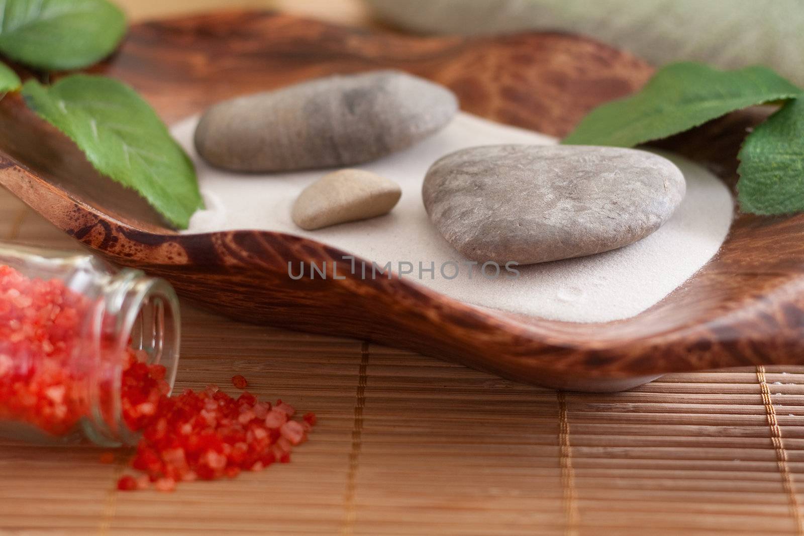 Massage stones on sand in a bowl and red bath salt