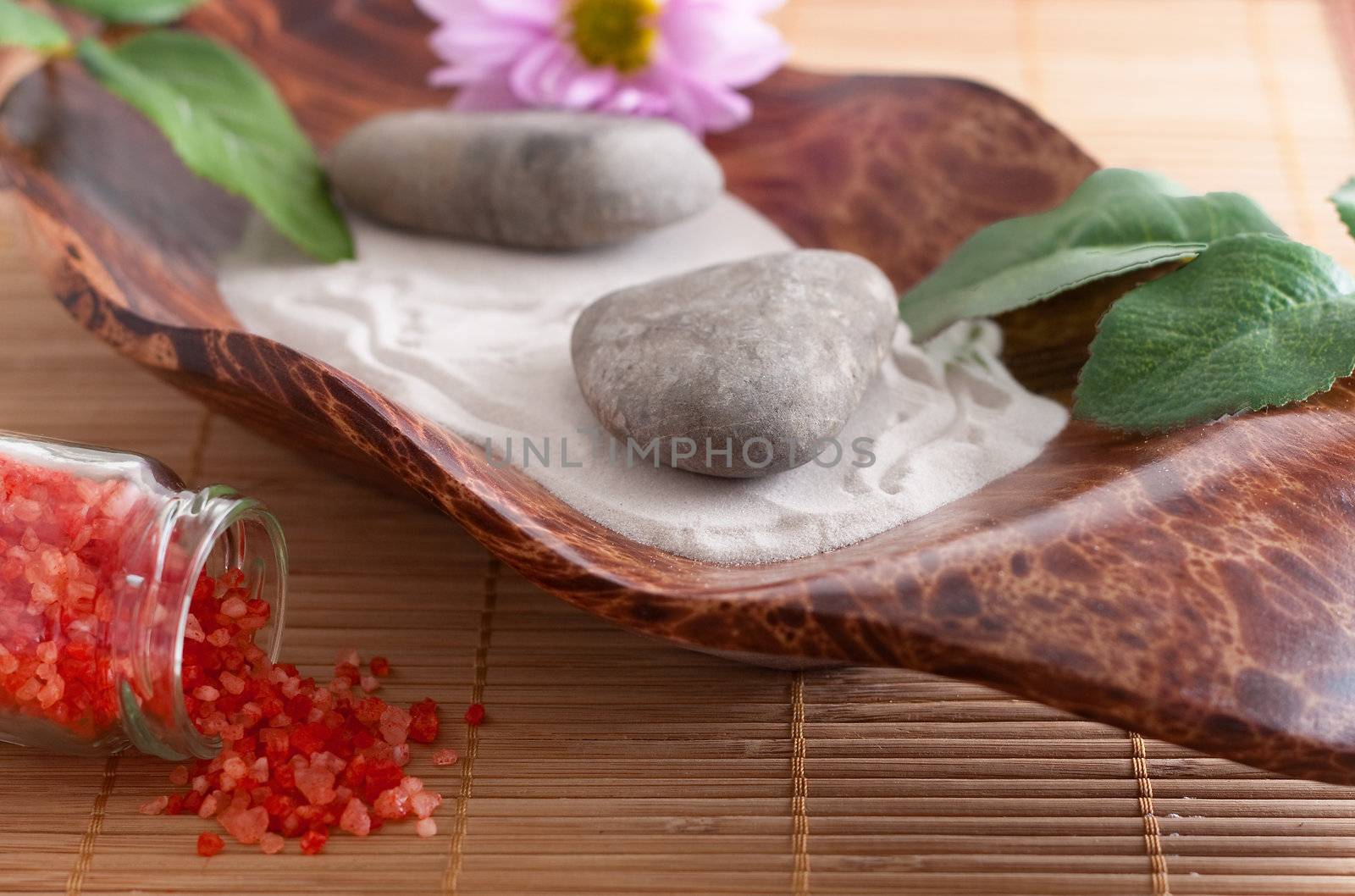 Massage stones on sand in a bowl, a purple flower and red bath salt