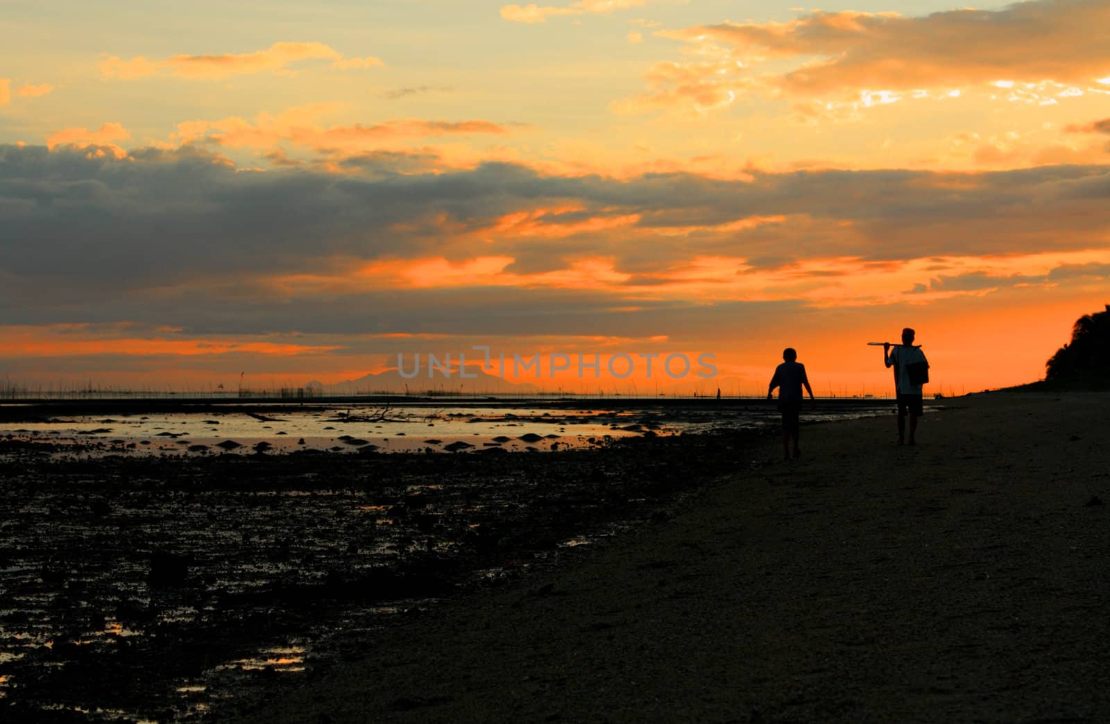 silhouette of a fisherman and his son walking on a low tide seashore