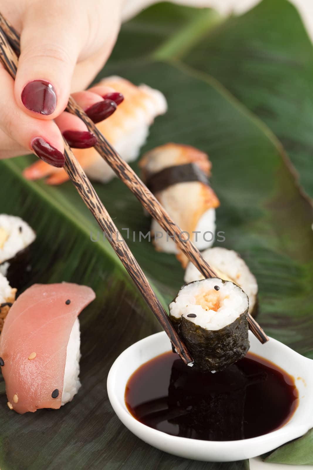 Woman hand with red fingernails holding chopstick to dip a sushi in the soy sauce