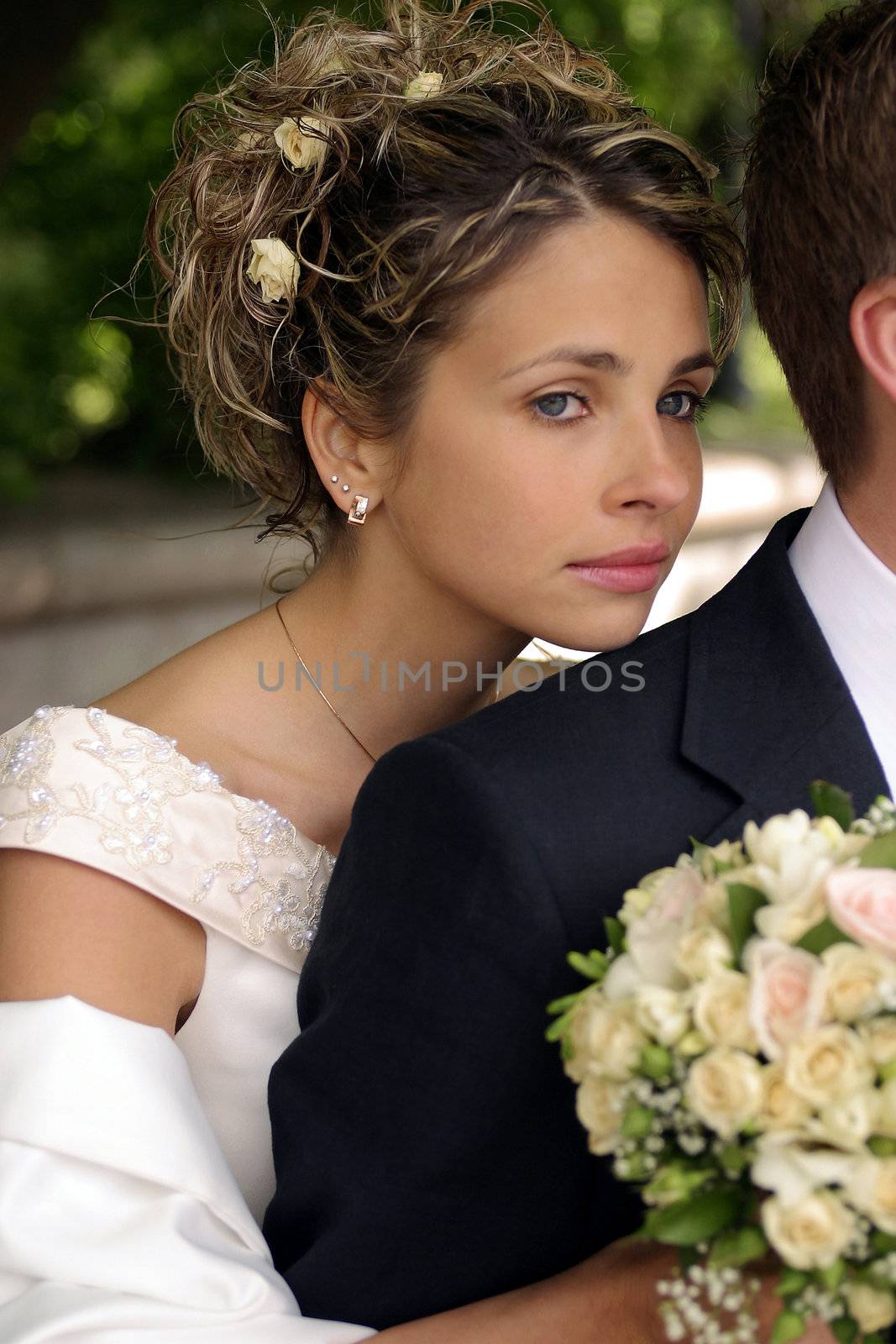 Pretty newlywed bride leaning on husbands shoulder with bouquet.