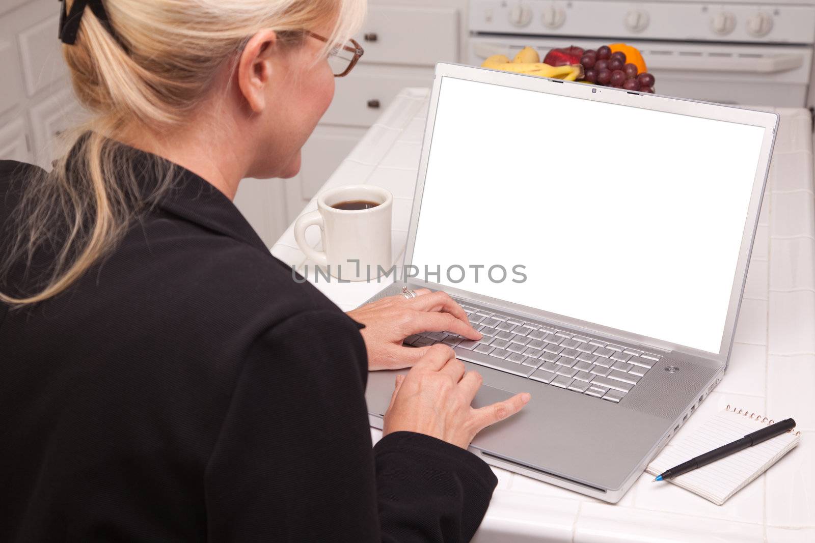 Woman Sitting In Kitchen Using Laptop with Blank Screen. Screen can be easily used for your own message or picture using the included clipping path.