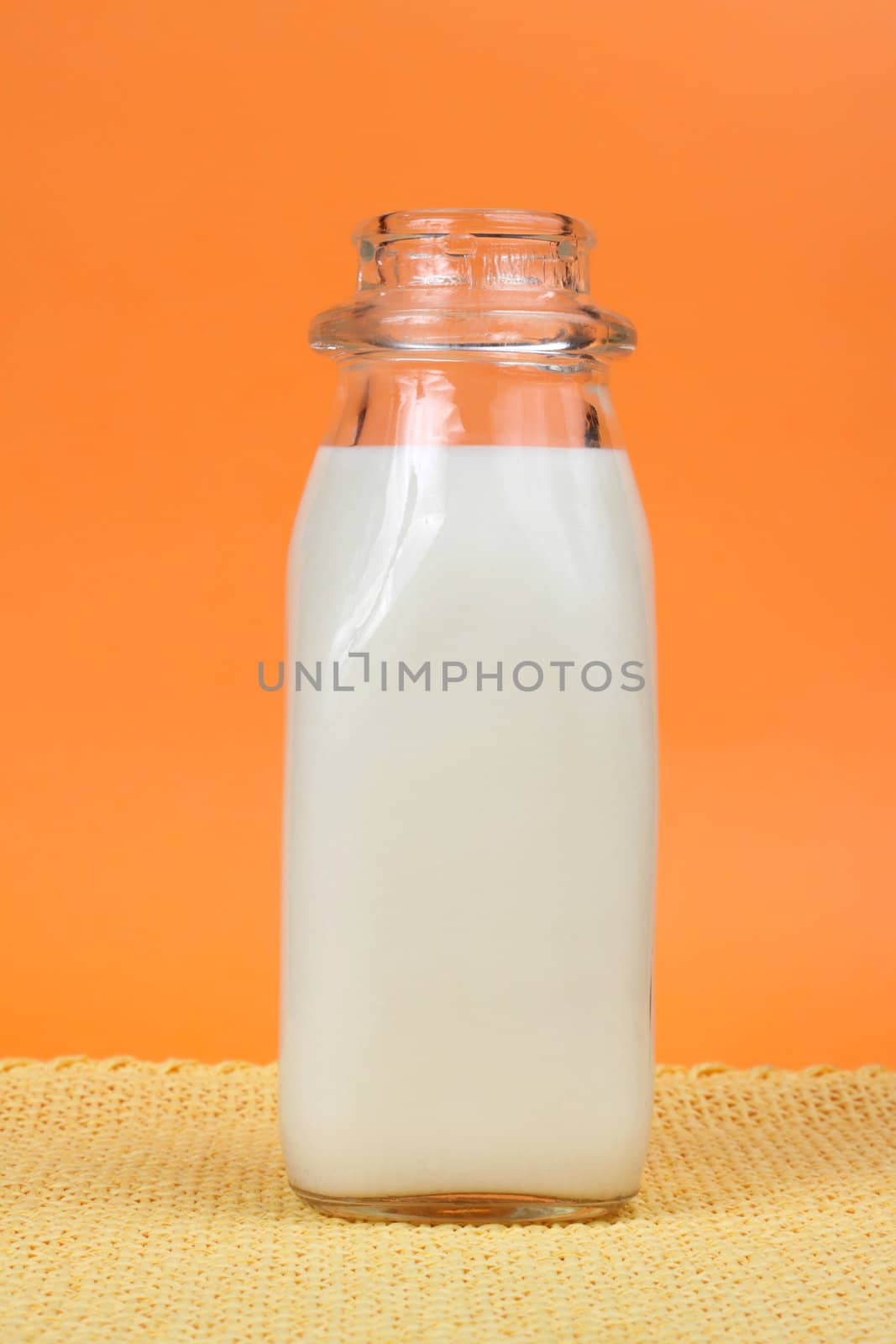 glass bottle filled with fresh milk, orange background