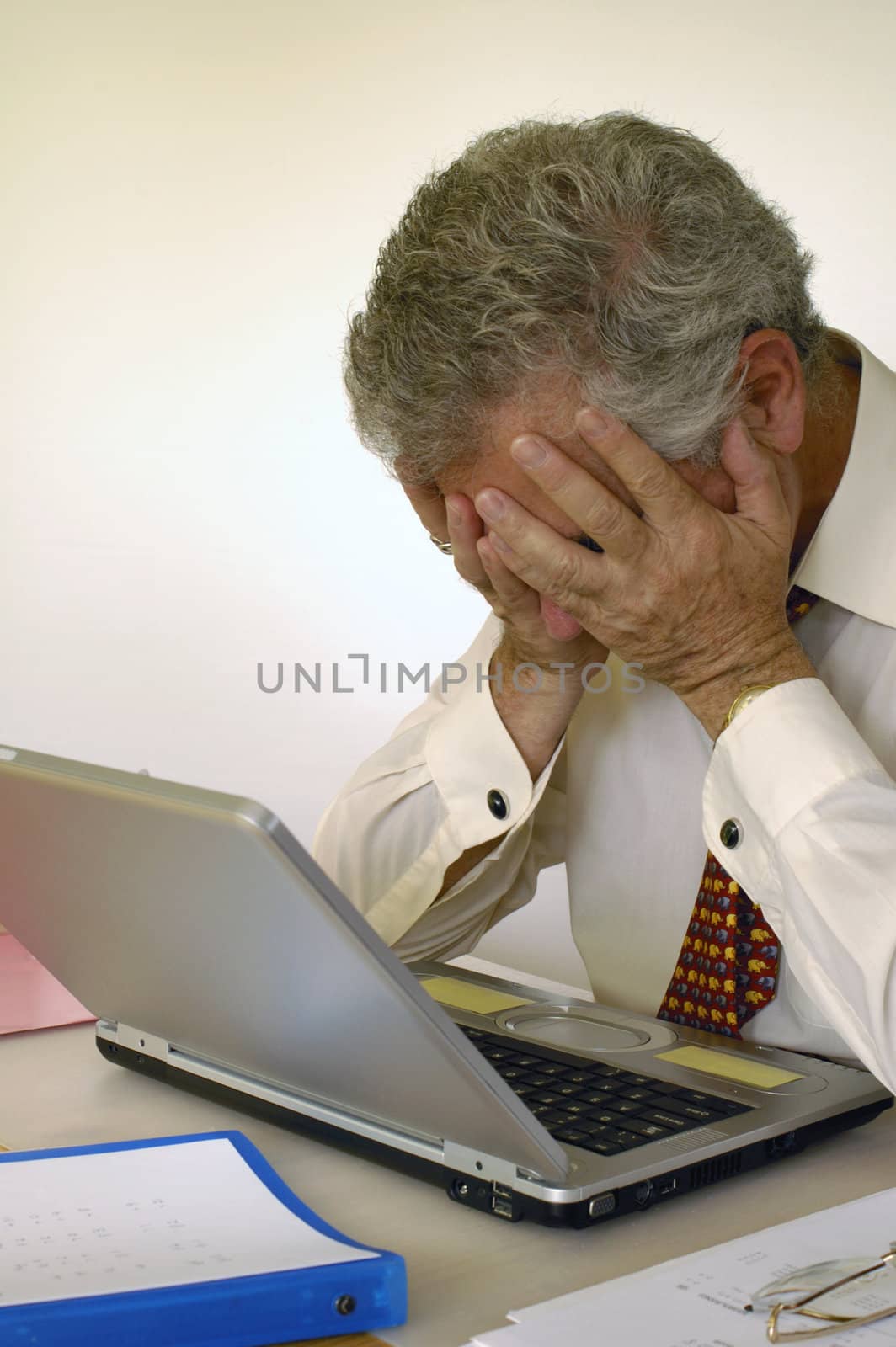 A businessman holds his head in his hands in front of his laptop computer, in despair. Space for text on the white background.