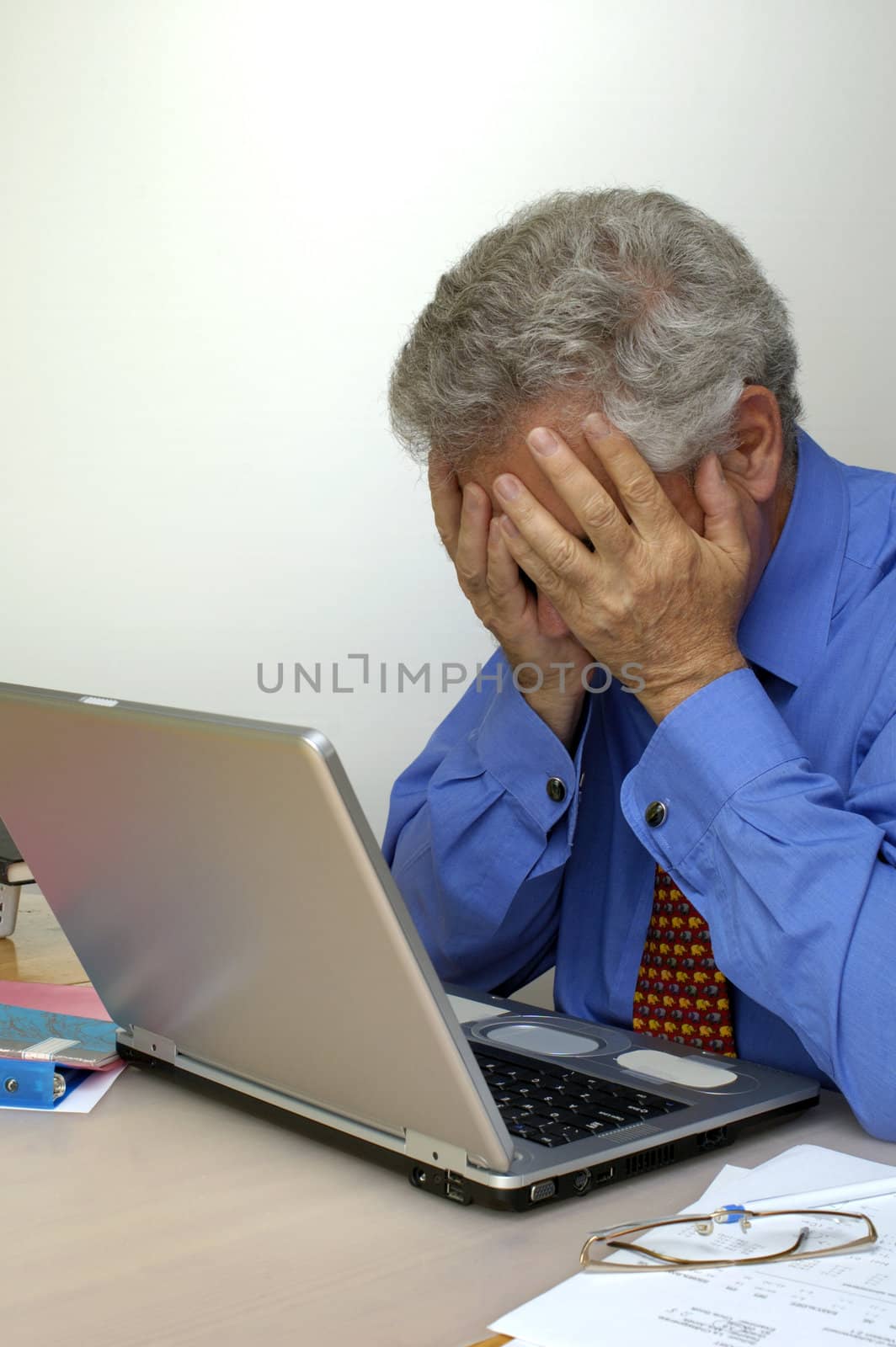 A businessman holds his head in his hands in front of his laptop computer, in despair. Space for text on the white background.