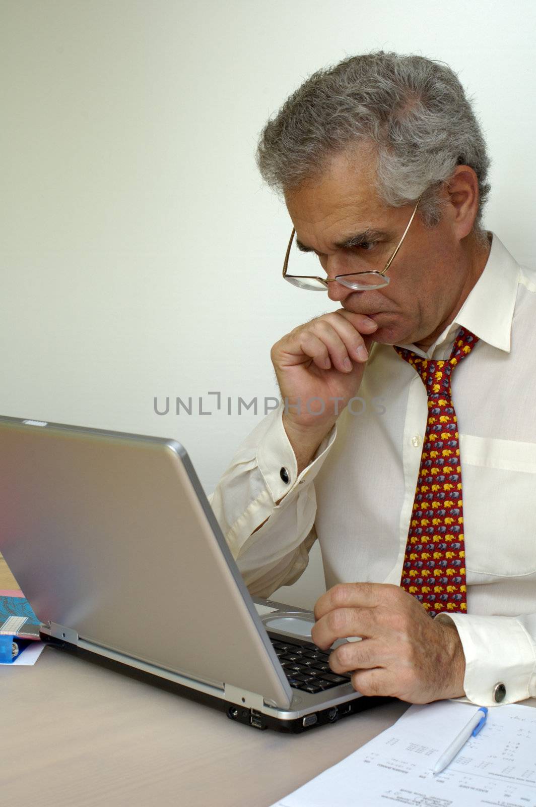 A mature businessman gazes at his laptop computer thoughtfully. Space for text on the white background.