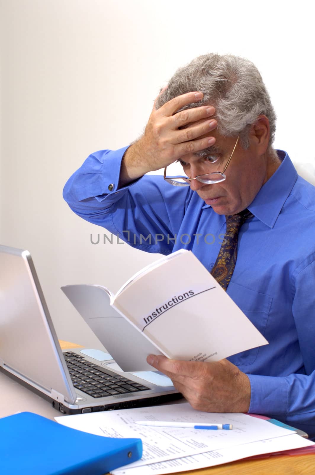 An older businessman clutches his brow as he gazes at the instruction booklet of his laptop. How does this thing work?