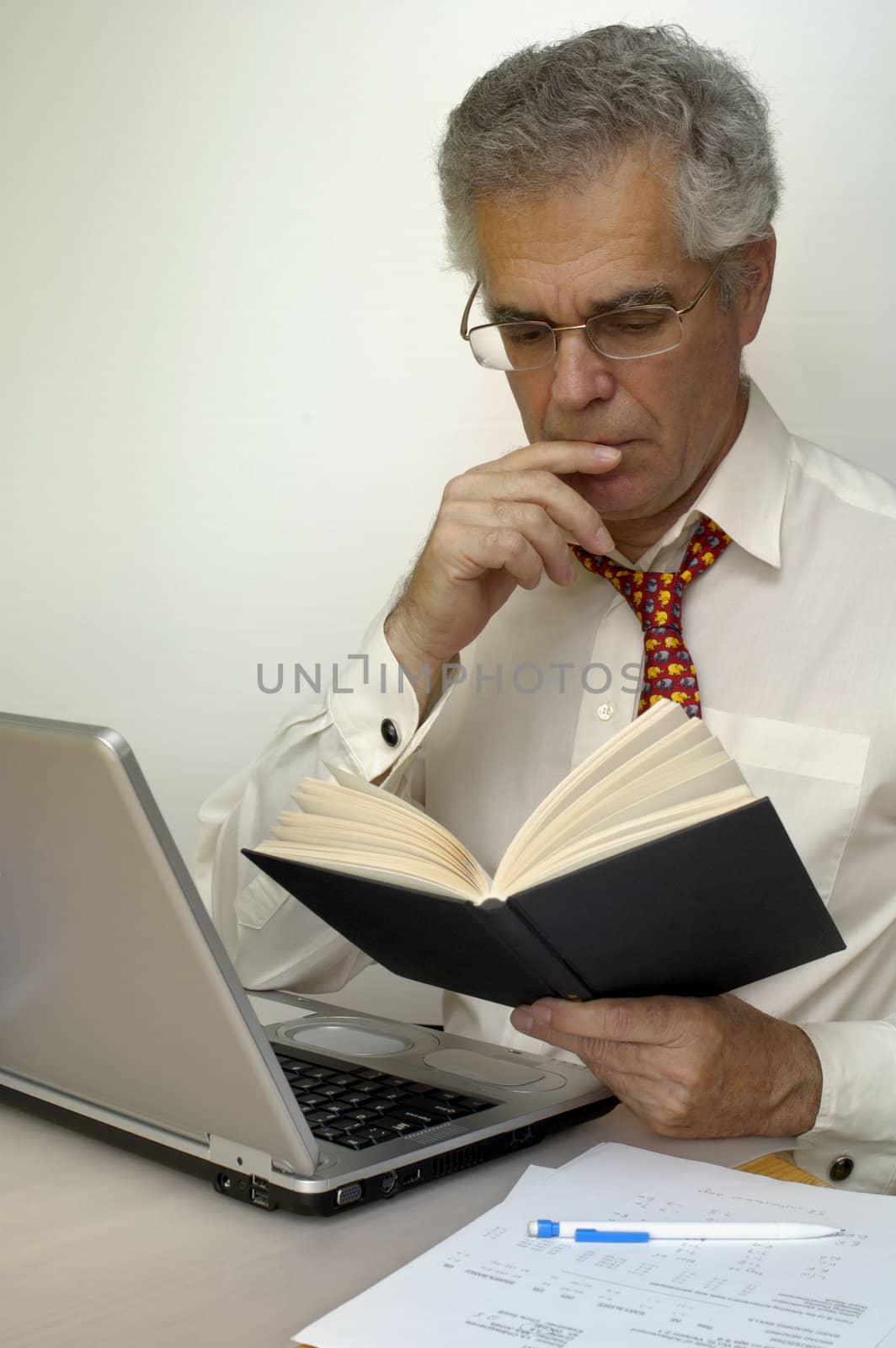 A businessman reads a book as he sits at his laptop.. Space for text on the white background.