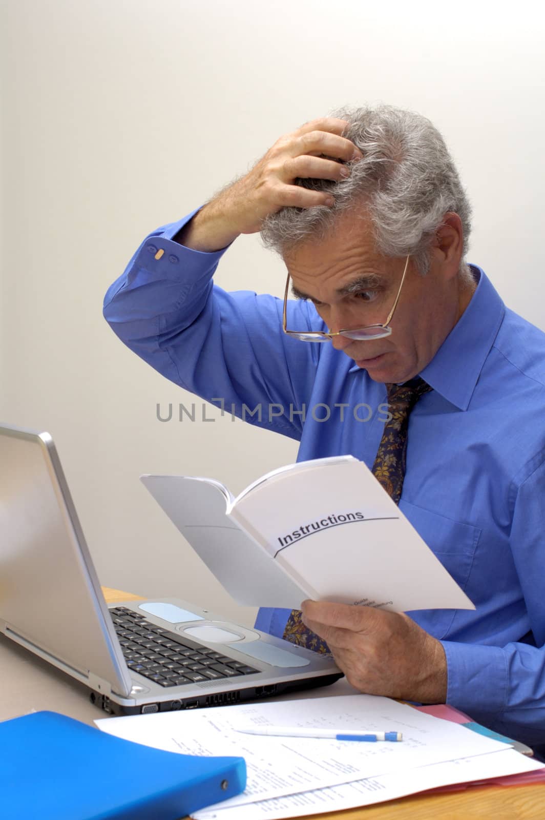 An older businessman gazes at the instruction booklet of his laptop, scratching his head in puzzlement. How does this thing work?