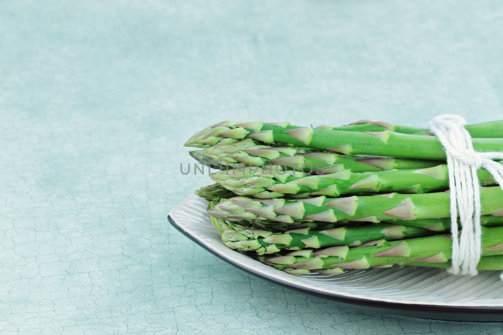 Fresh asparagus tied in a bundle against a blue background with room for copy space.