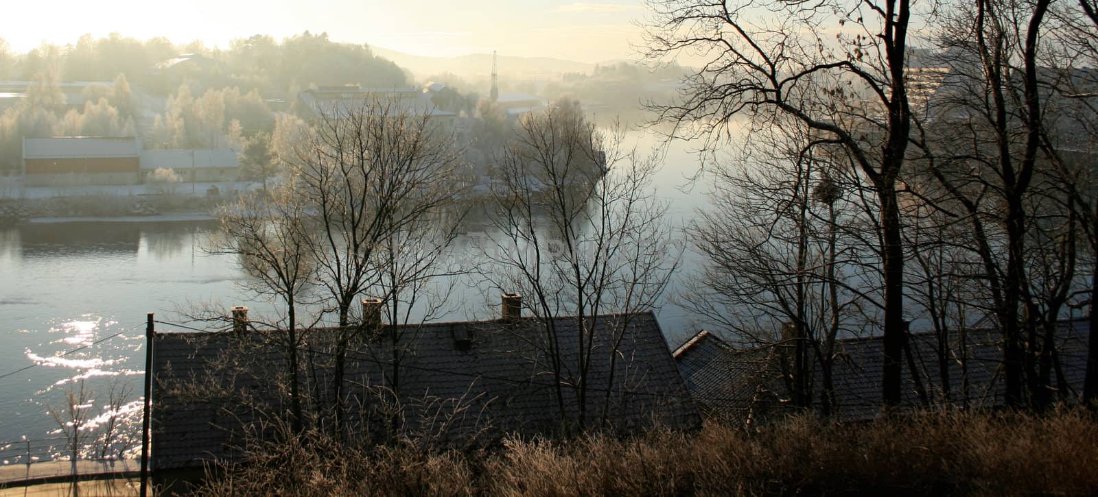 View over a foggy river, roof in the front, trees with some houses in the background