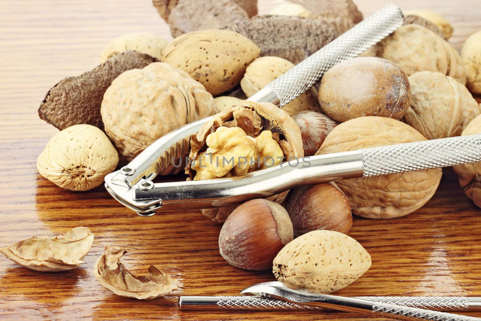 Mixed nuts and a nut cracker on a wooden table with reflection in wood. Shallow depth of field.