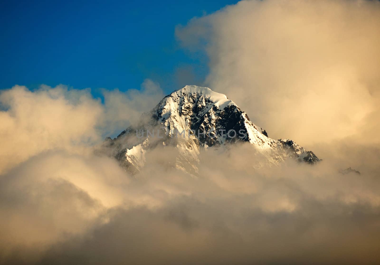 A Mountain peak in Alaska near Matanuska Glacier peaks through the clouds at sunset.