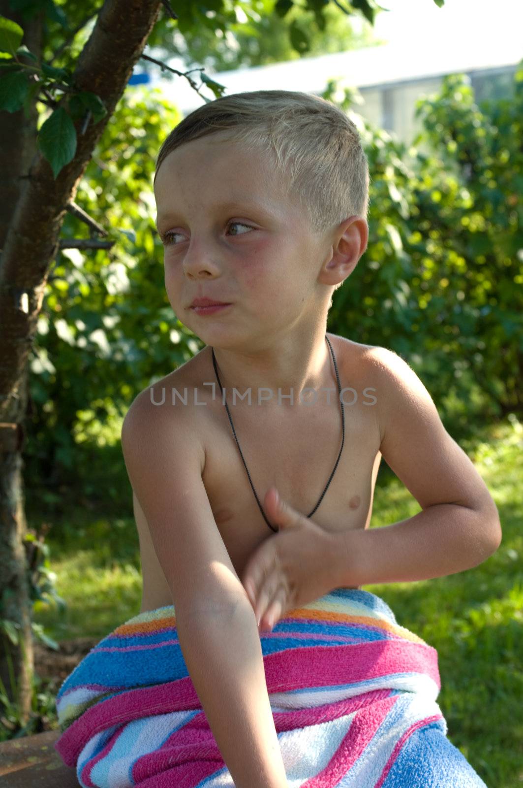 Child sits under a tree turned in  towel in the solar summer evening
