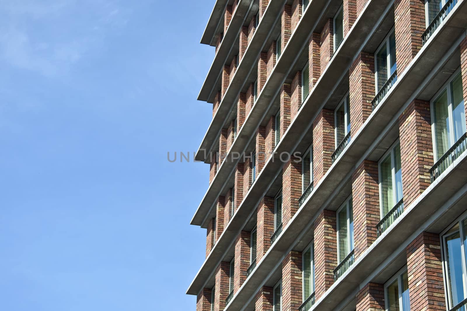 Fragment of the facade of the modern brick residential house with the same balcony. Detail. Against the blue sky.