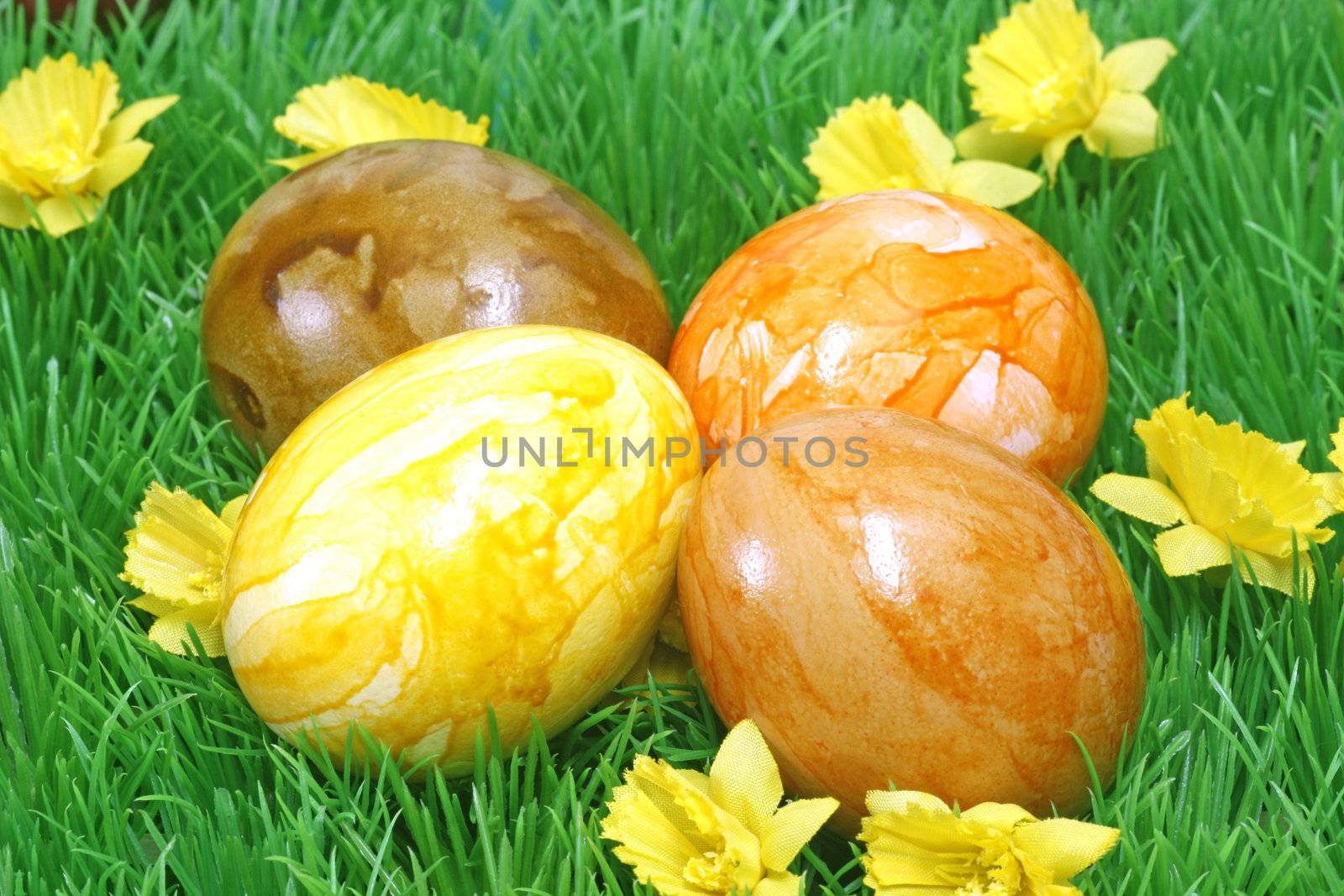Four coloured easter eggs on grass with flowers