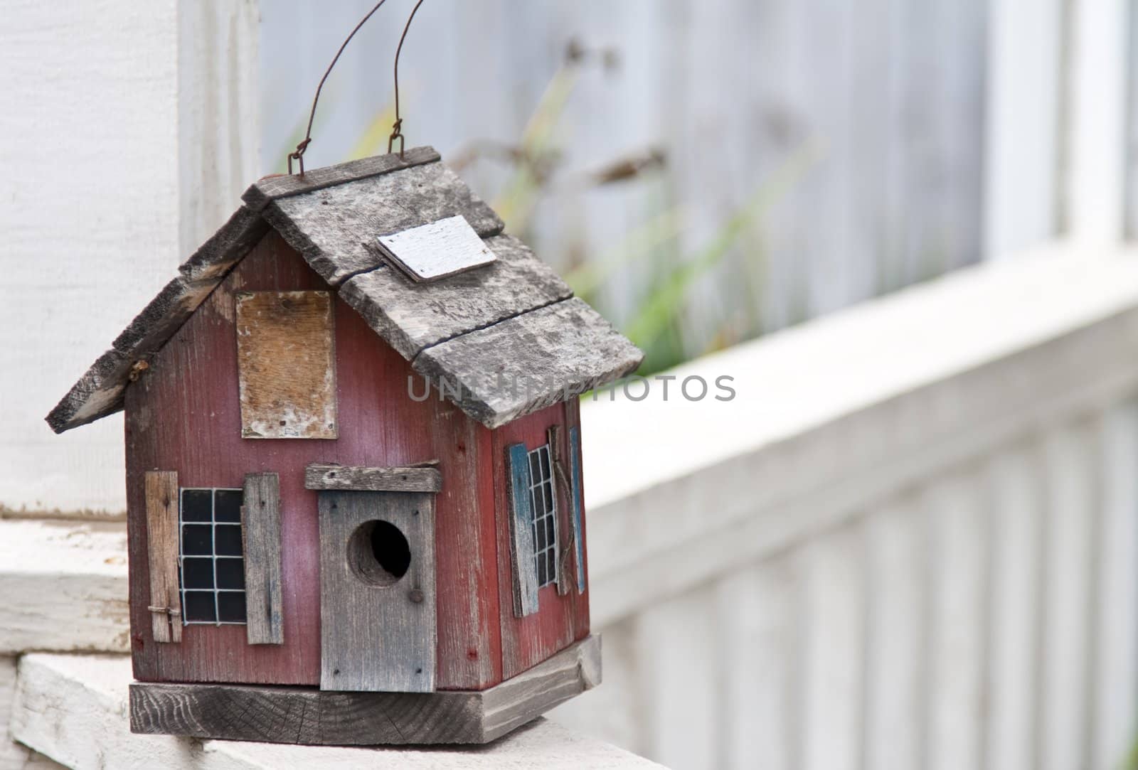 Country folk style bird house on front porch railing