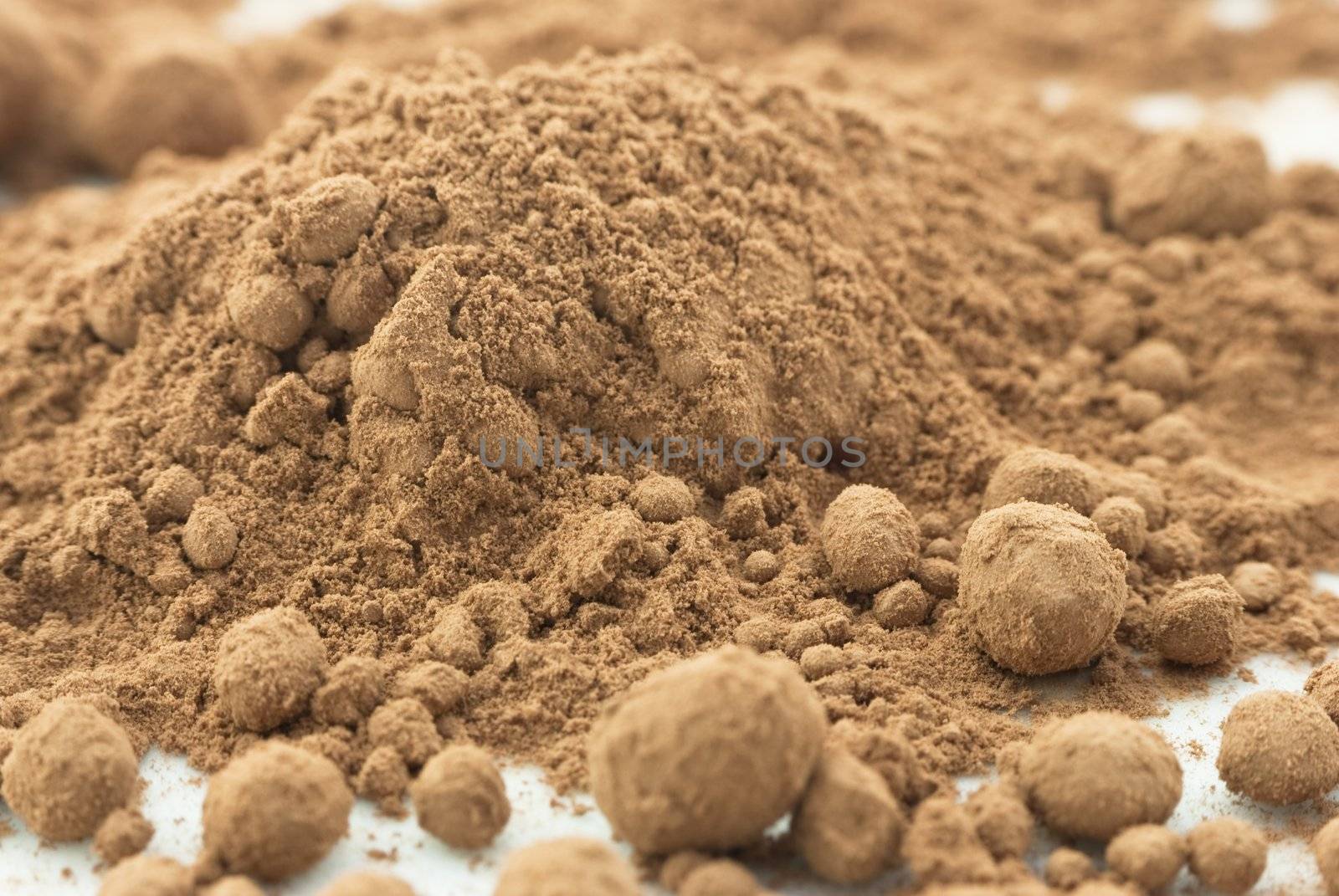 Macro (close-up) of cocoa powder, scattered on white surface and forming the shape of a mountain.  Some powder has beaded and formed into balls.