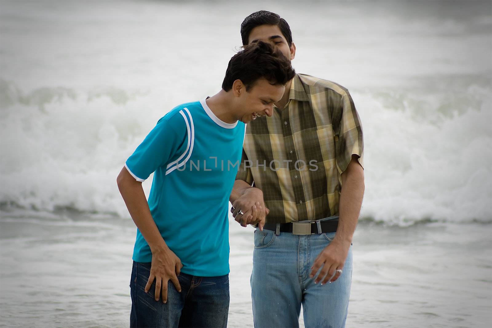 Two men standing on a beach at the shoreline, chatting and watching something