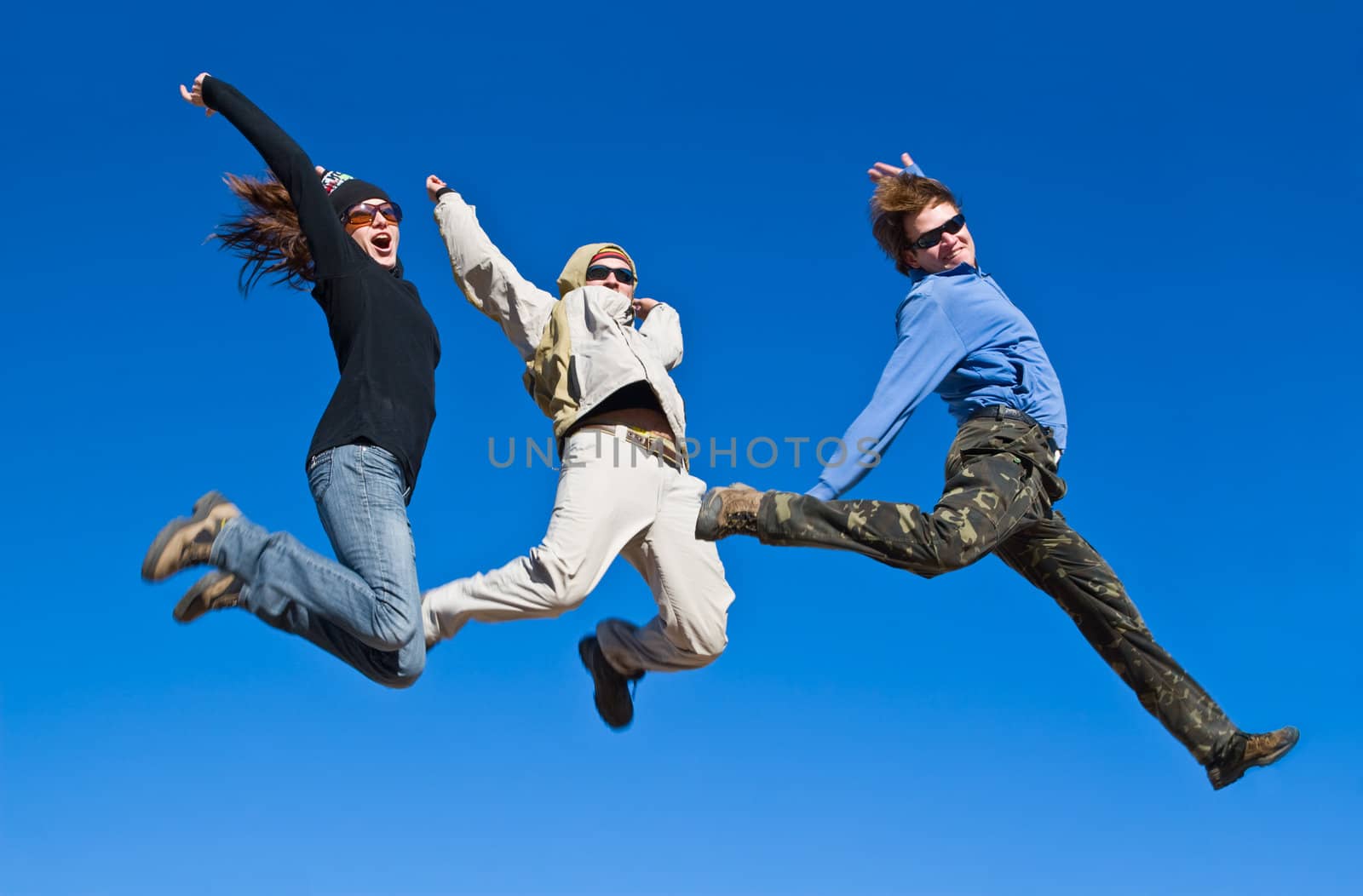 Three hikers jumping cheerfully on mountain summit in clear sunny weather