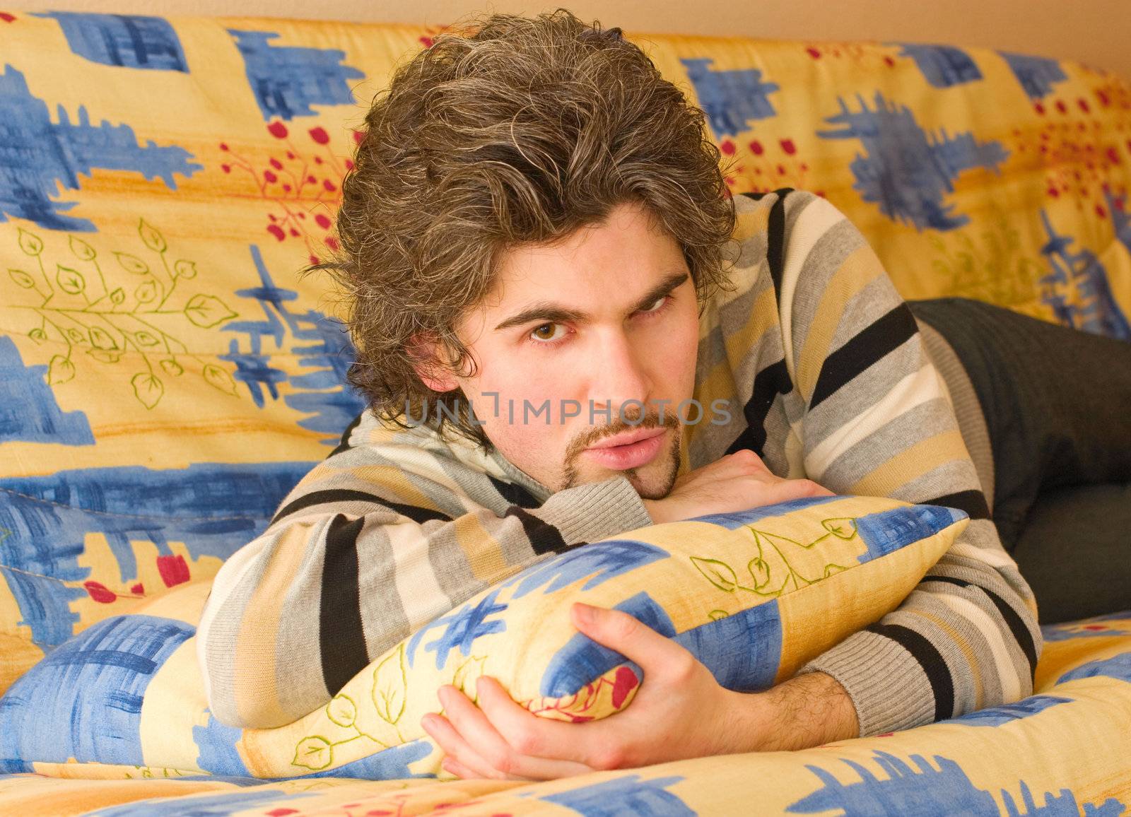 Young serious dark haired caucasian man in striped sweater lying on country style sofa