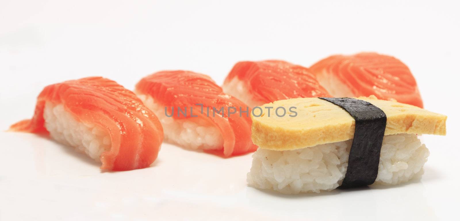Sushi isolated against a white background.The closest is egg sushi(tamago) and in the background there are four salmon sushi.