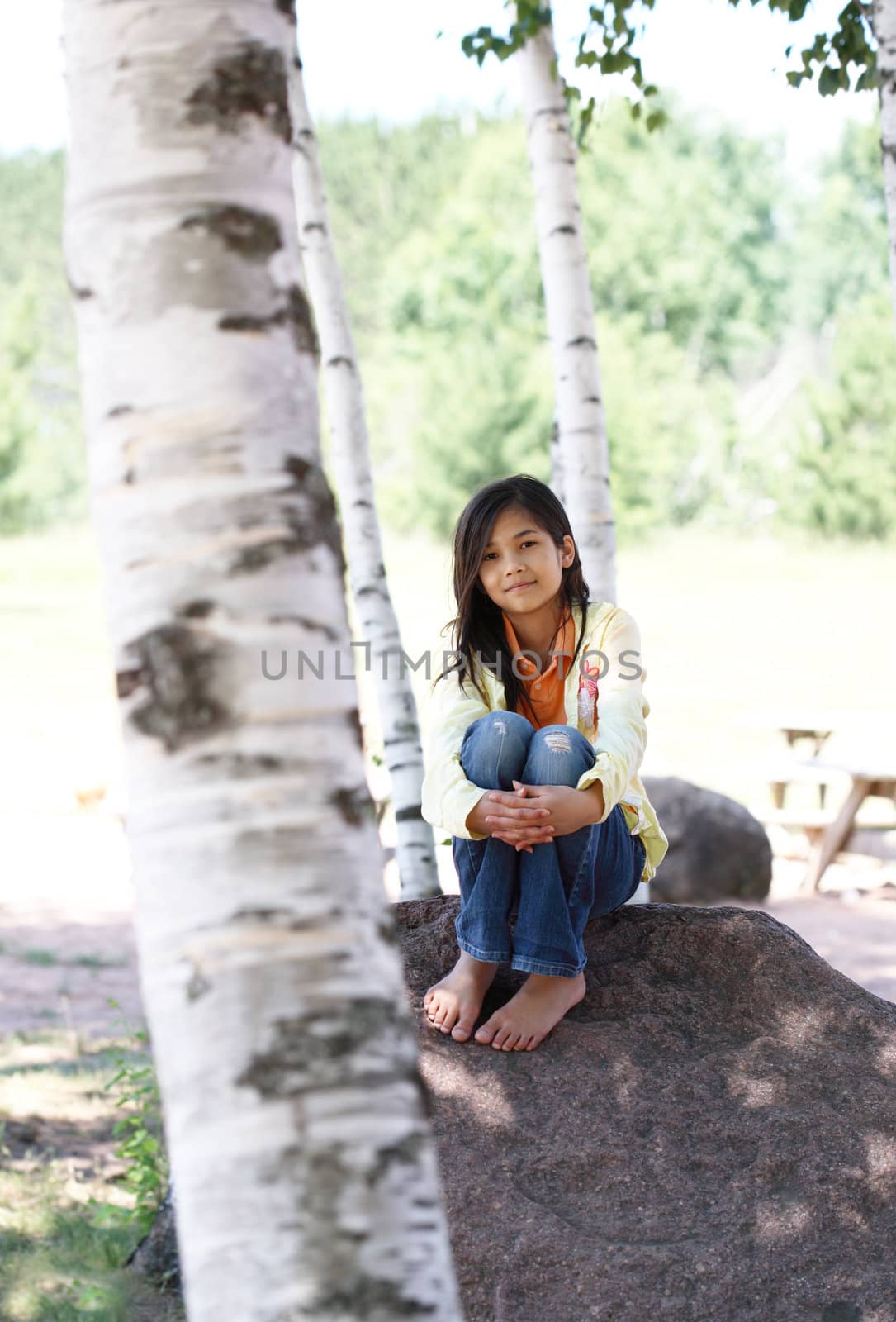 Little girl sitting under birch trees