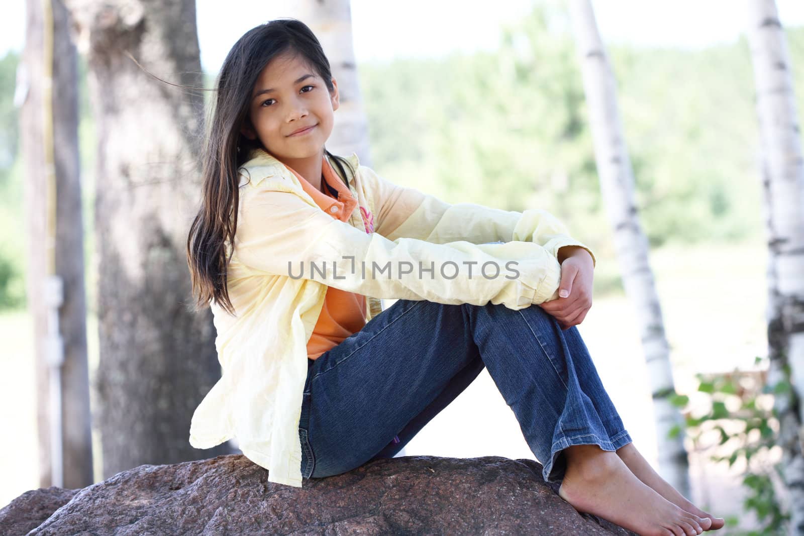 Little girl sitting under birch trees