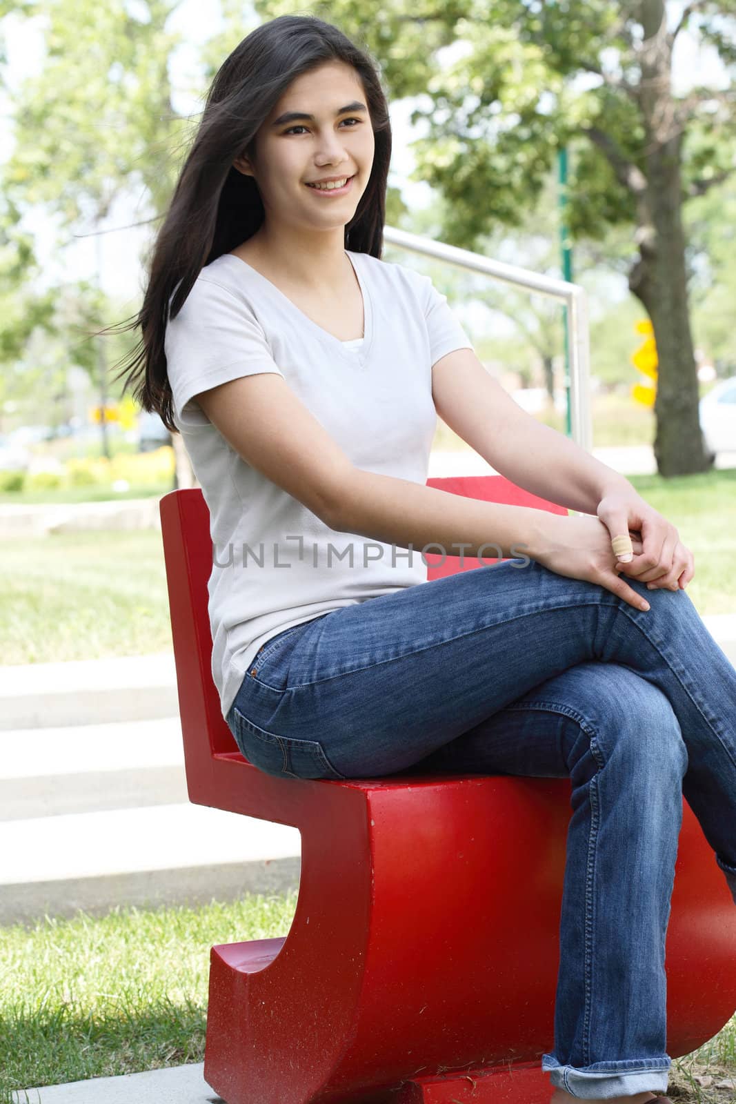 Beautiful teen girl sitting outdoors on red chair in summer