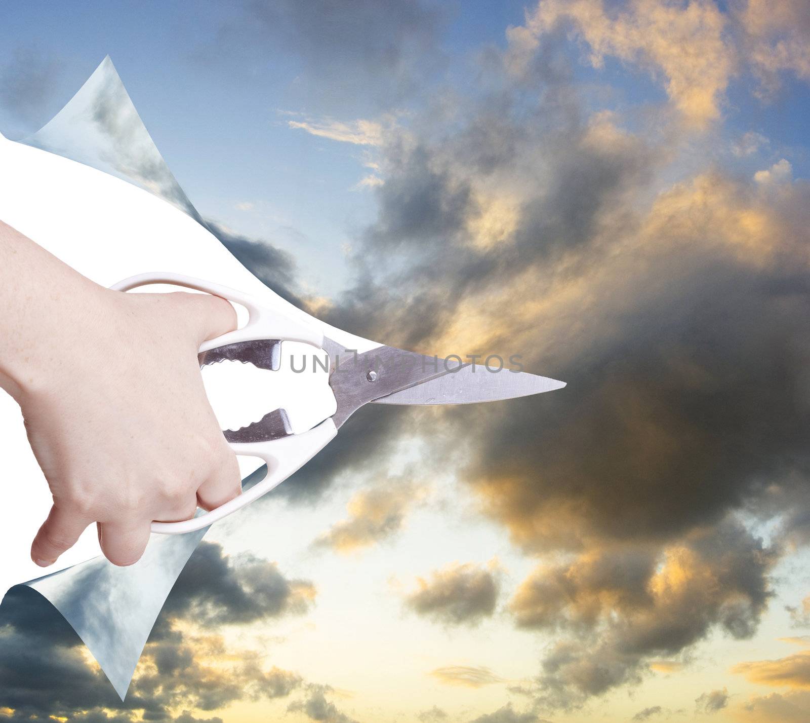 hand with scissors cutting the paper to reveal the sky