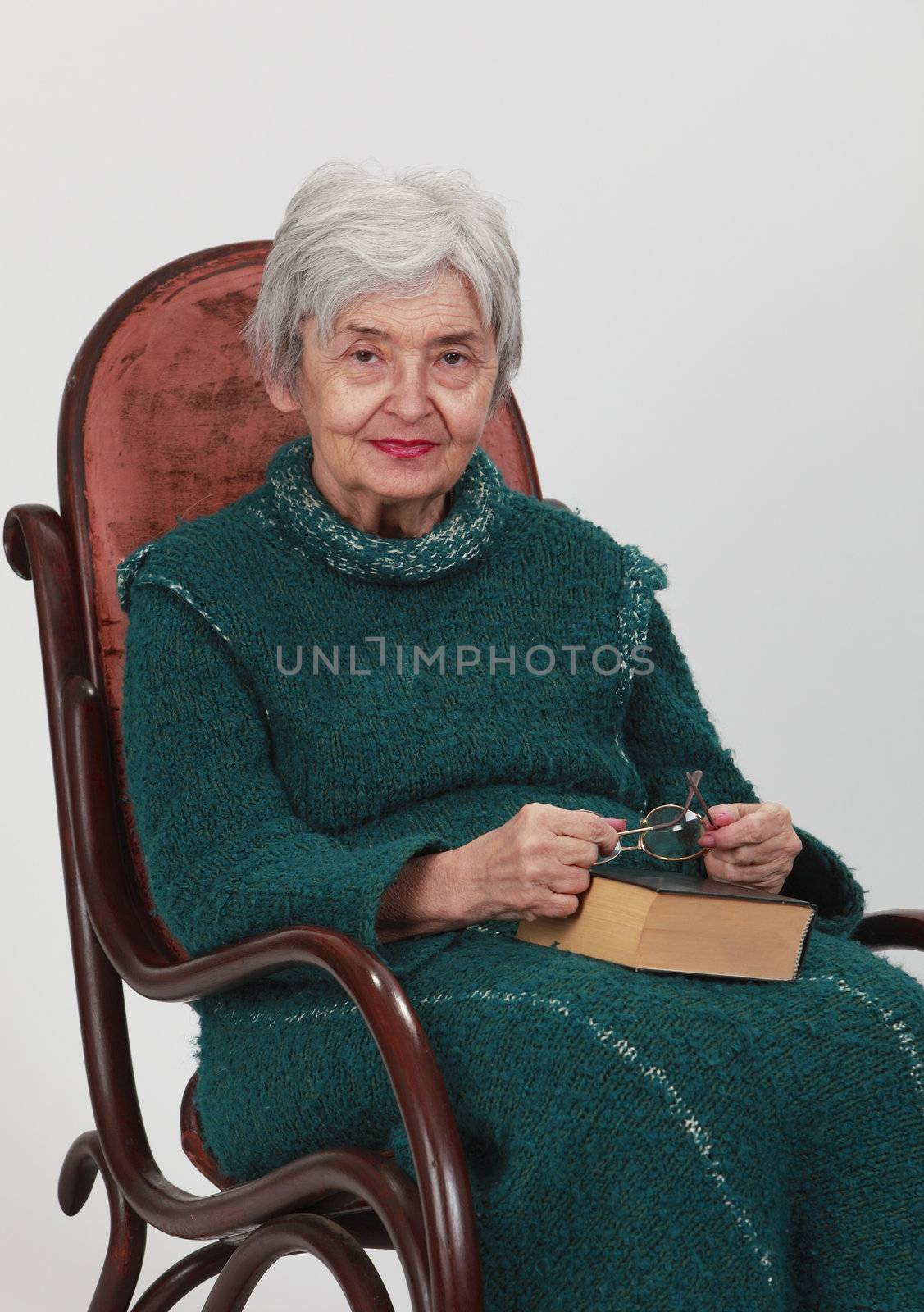 Image of an old woman sitting on a rocker with a closed book and her glasses in her lap.