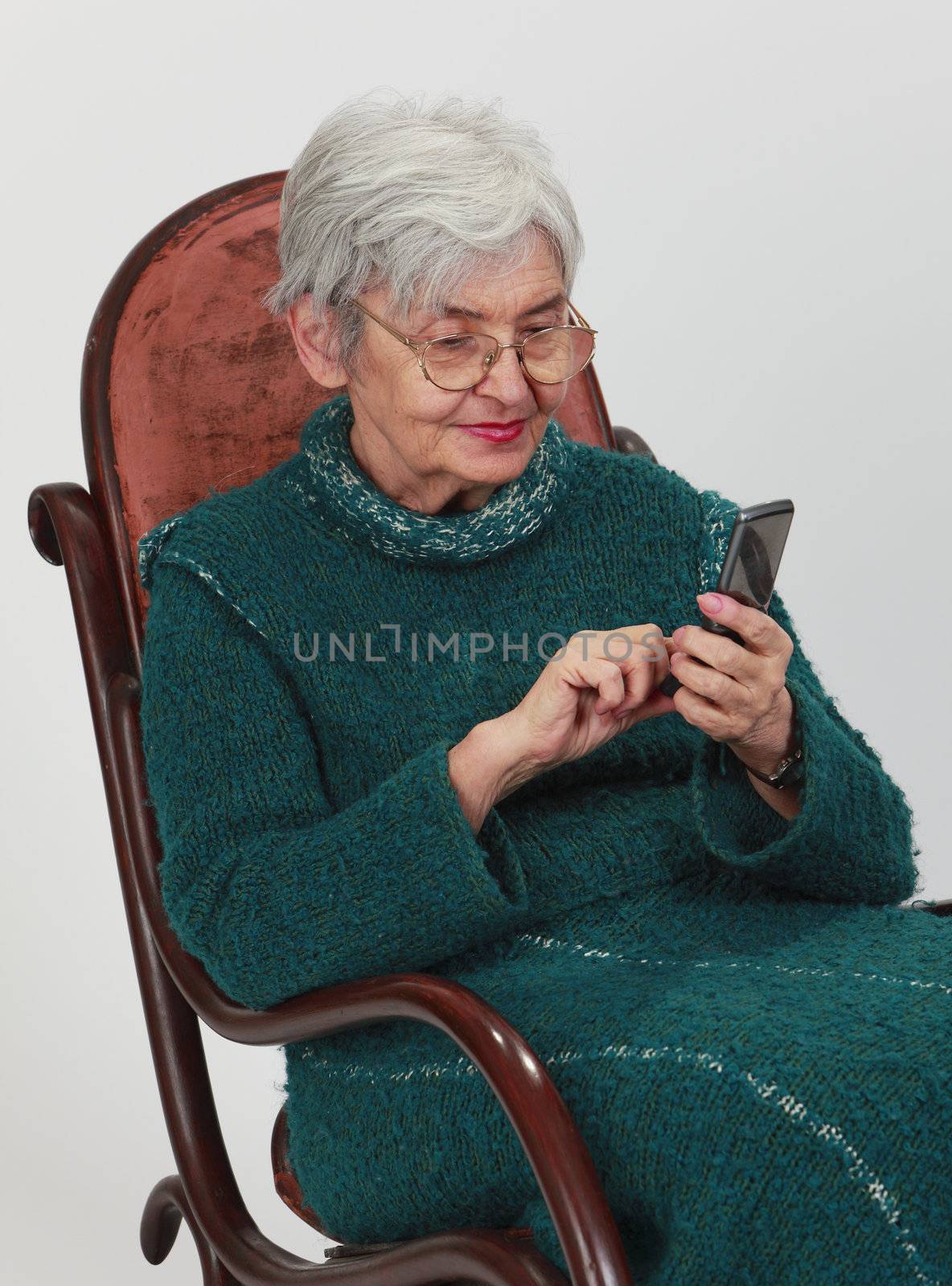 Close up image of a senior woman siting in a rocker and writing a phone message.