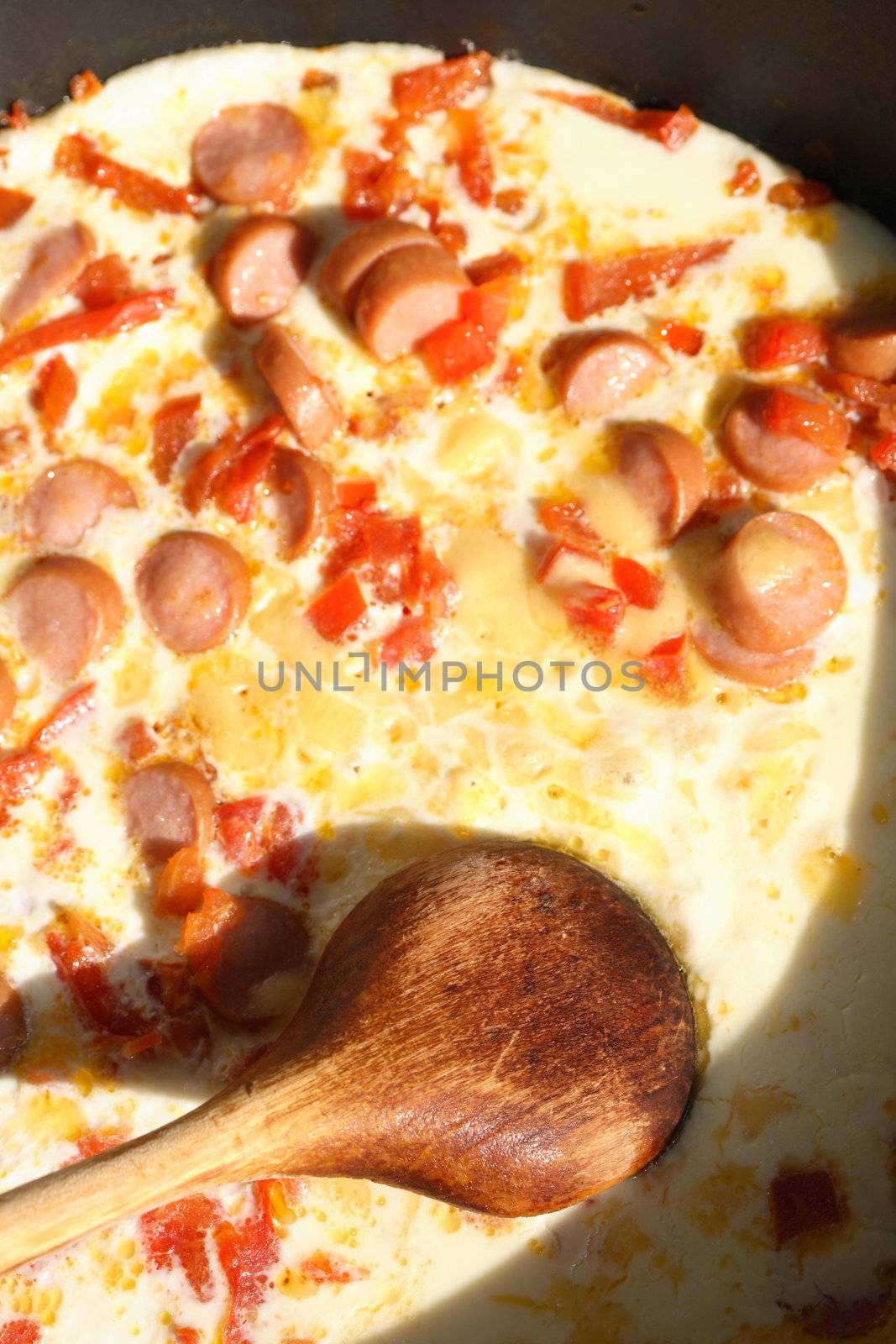 Closeup of scrambled eggs with sausage and wooden spoon