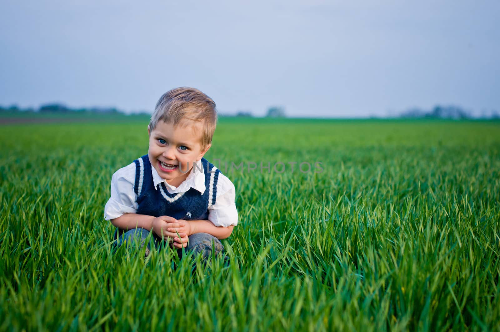 A beautiful little boy sitting in the grass by maxoliki