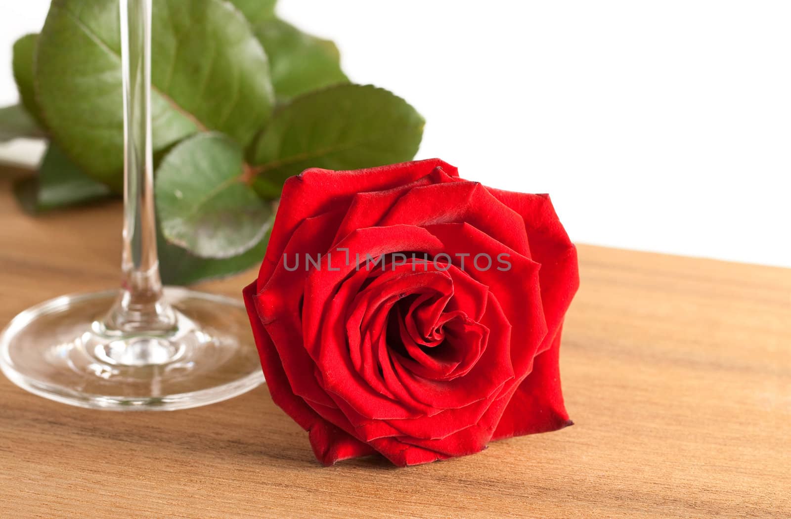 A red rose and a wine glass on a wooden bottom isolated on white background