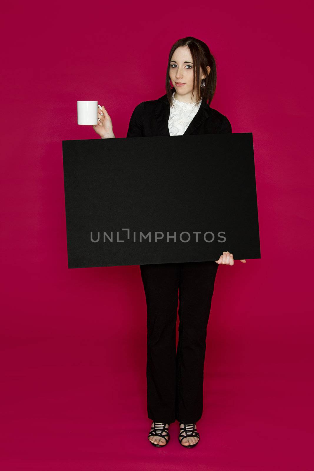 Young business woman holding a black board and a coffee cup with an inquiring expression against pink background