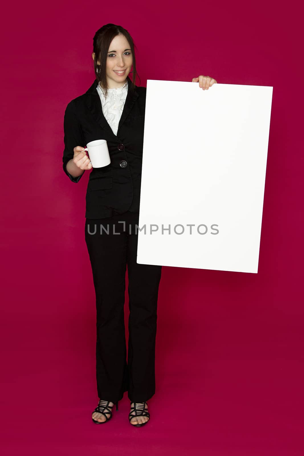 Young business woman holding a white board and a coffee cup against pink background
