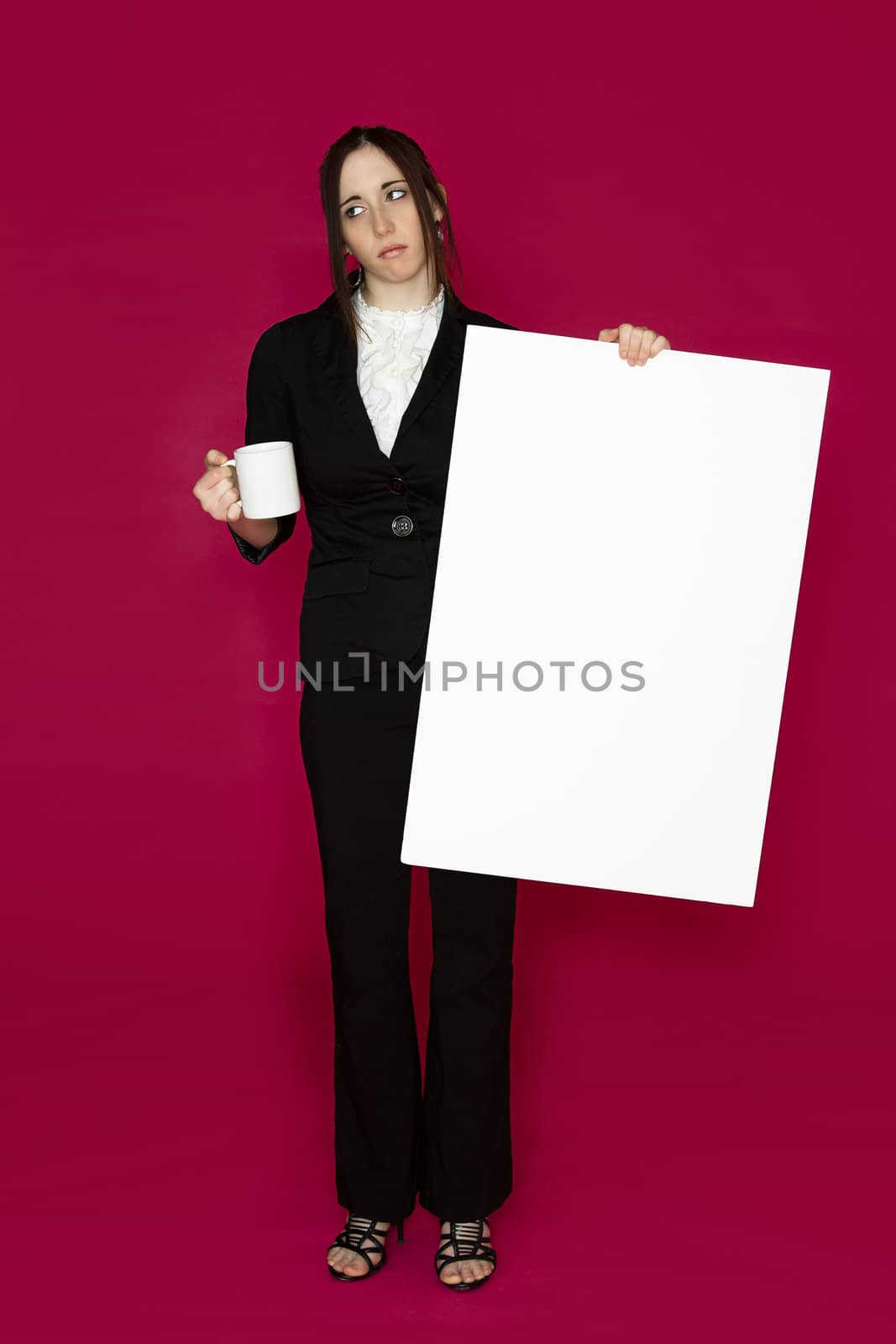 Young business woman holding a white board and a coffee cup with an inquiring expression against pink background