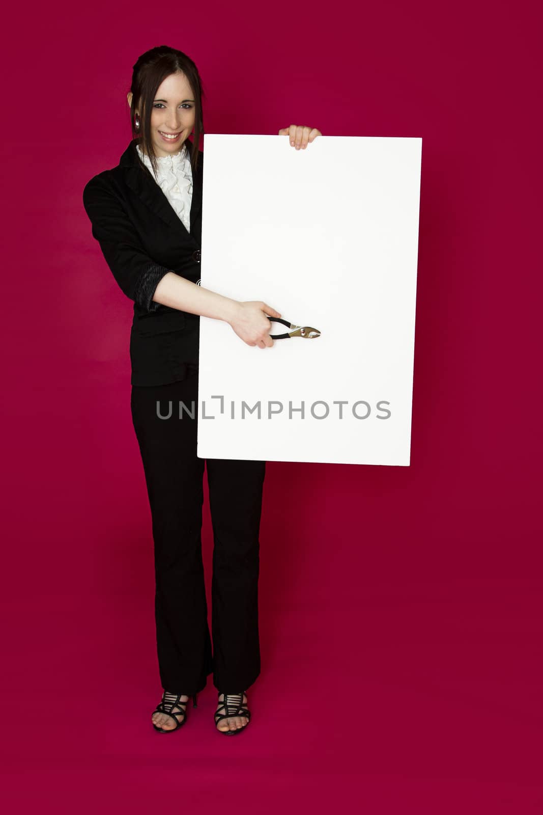 Young business woman holding a pair of plier pointing to a white board  against pink background