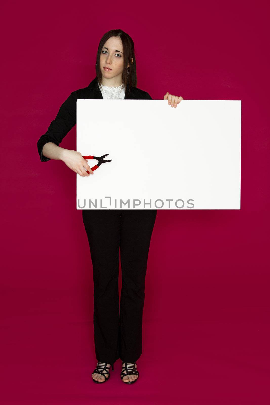Young business woman holding a pair of pliers pointing to a white board  against pink background