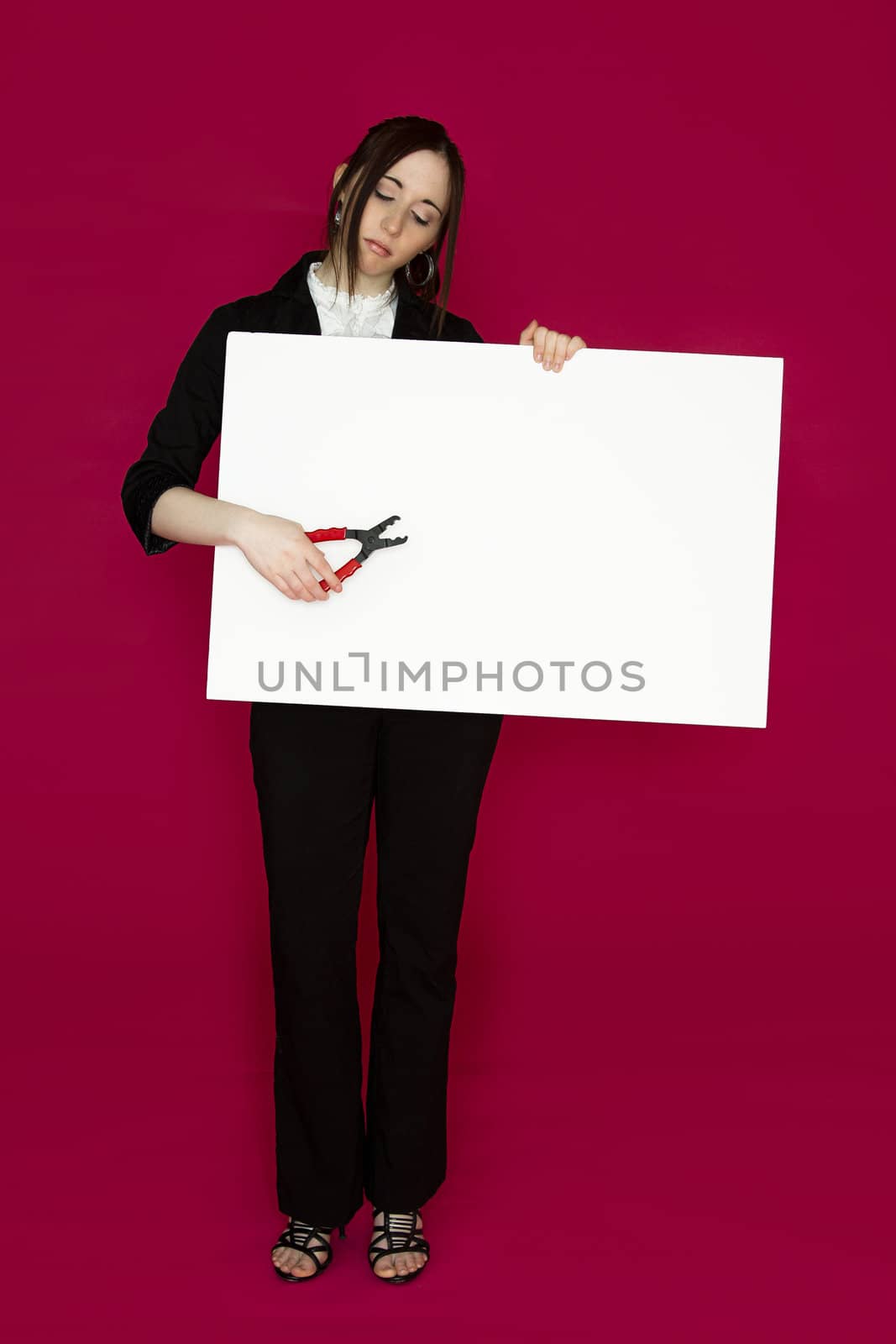 Young business woman holding a pair of pliers pointing to a white board against pink background