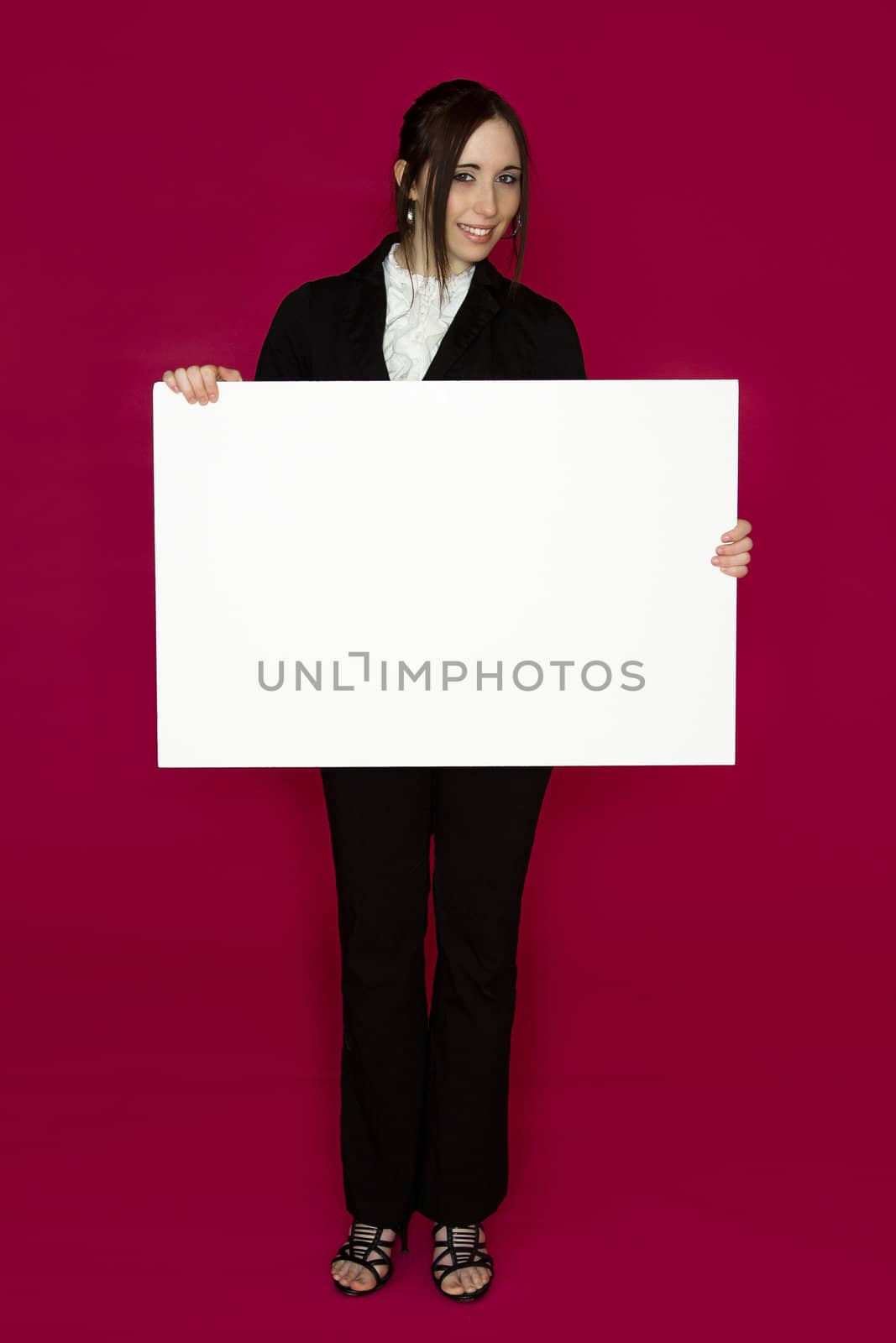 Smiling young business woman wearing a business suit standing behind looking down at a white board against pink background