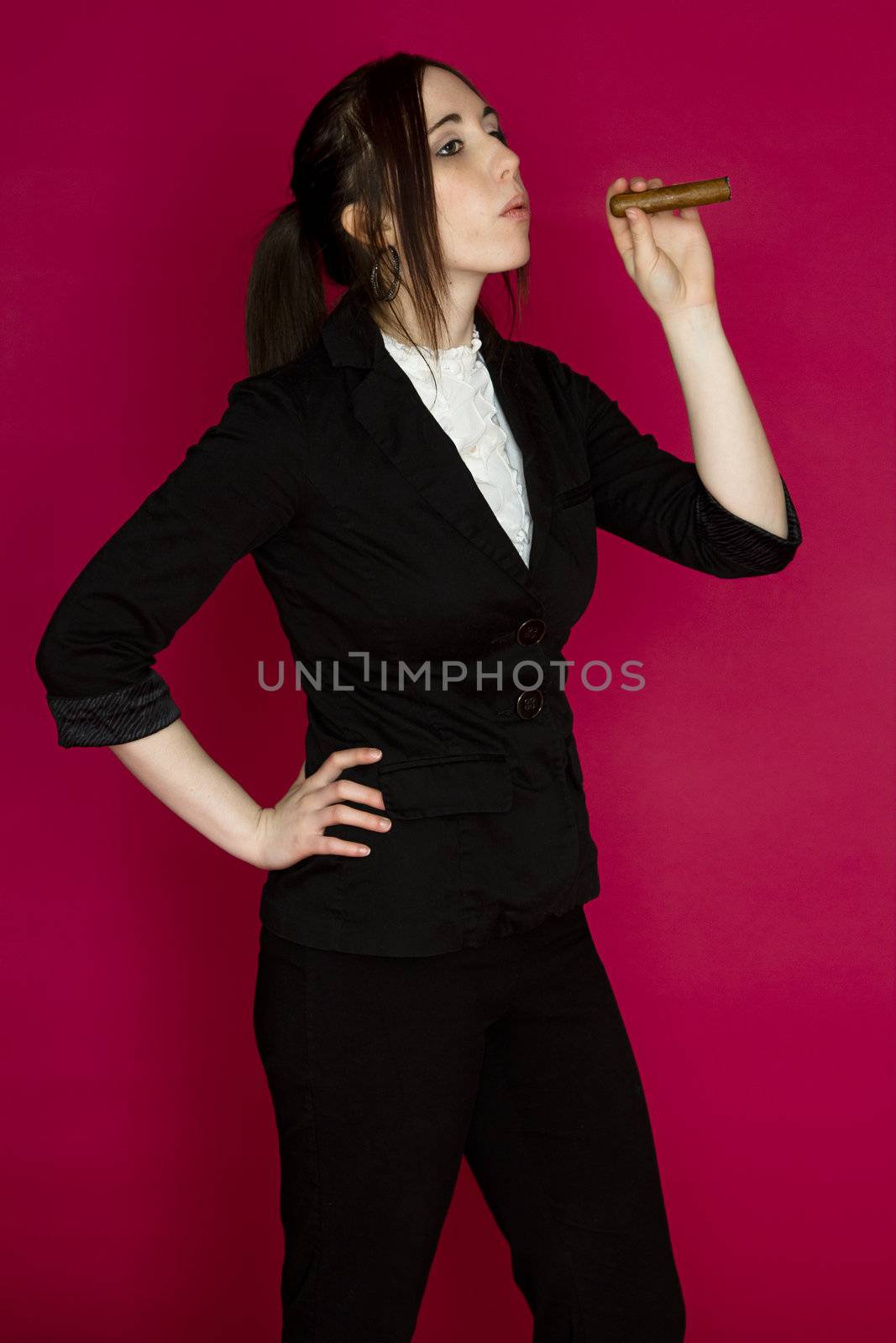 Young woman in a business suit blowing smoke from a cigar against a pink background